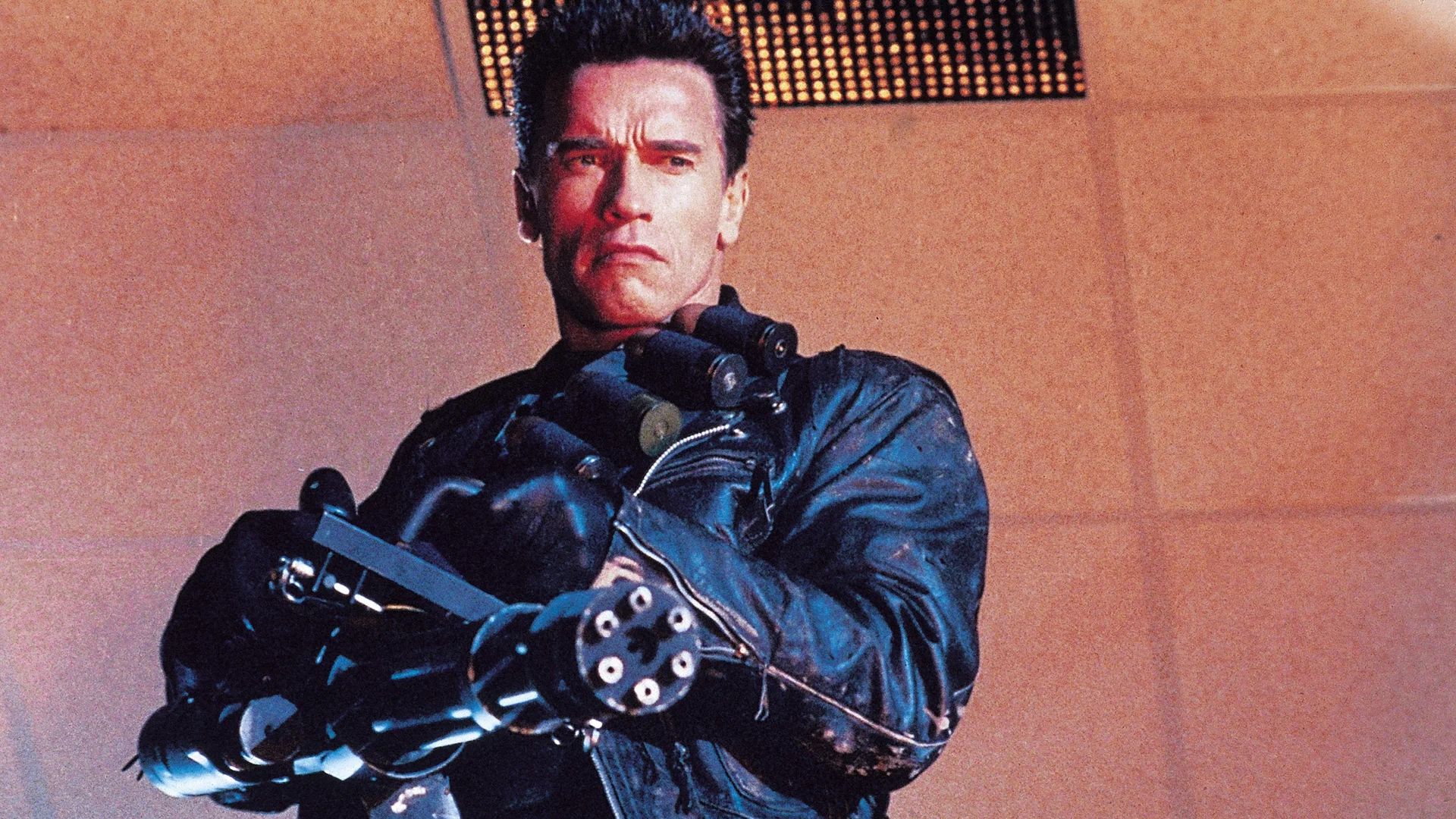 Arnold Schwarzenegger in a black leather jacket holding a minigun