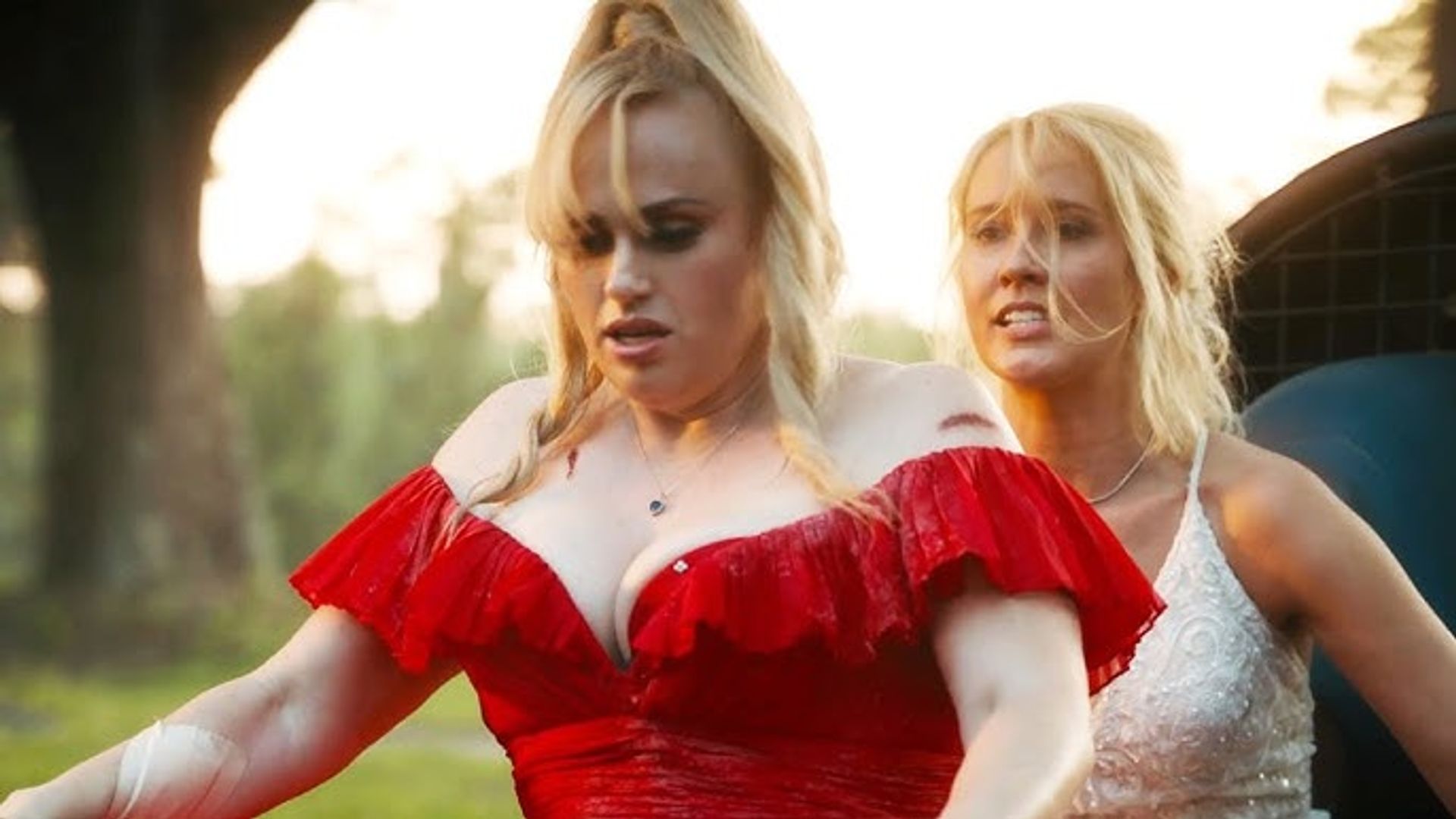 Rebel Wilson in a red dress and Anna Camp in white riding bicycles