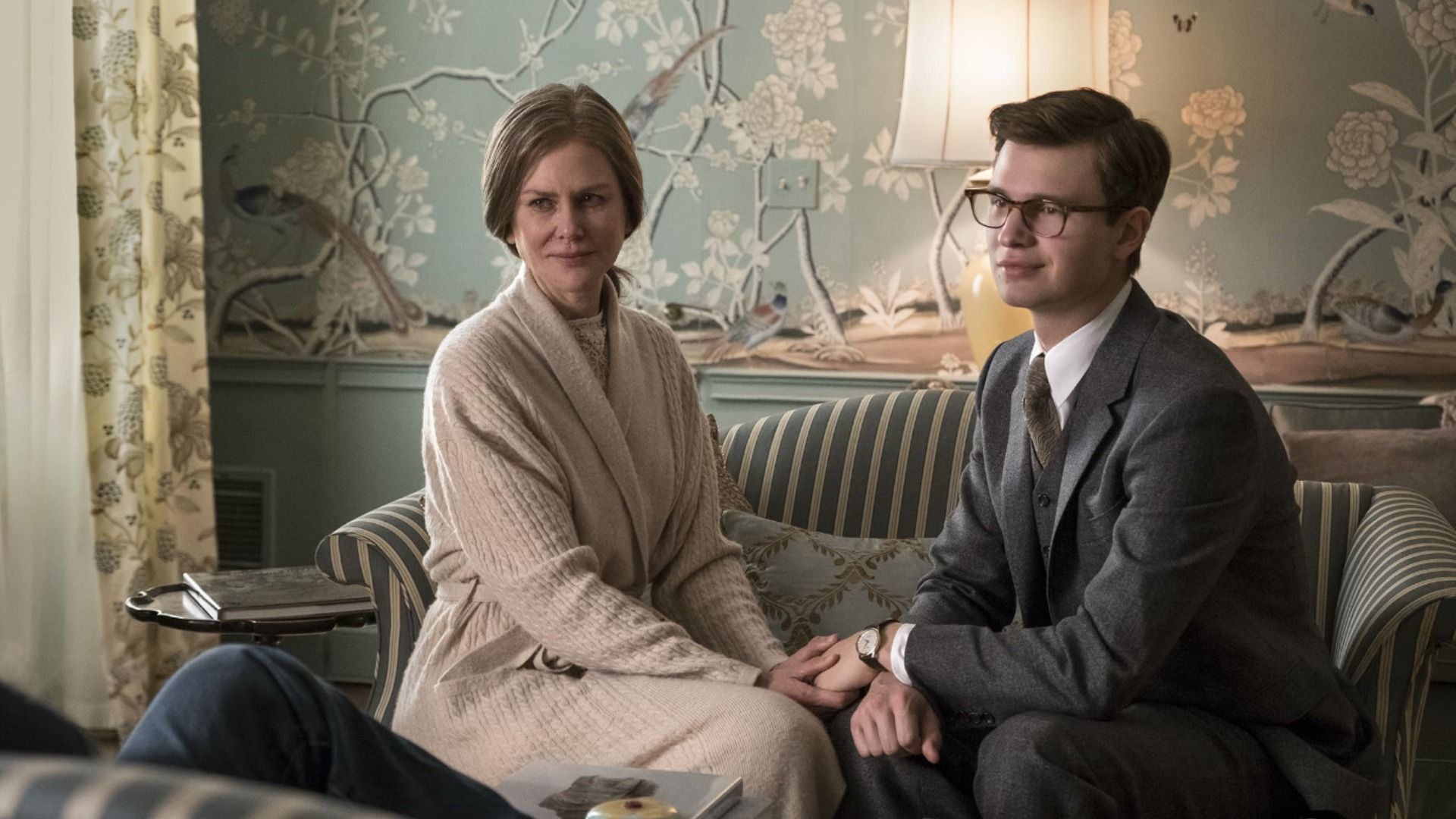 Actress Nicole Kidman in a white dress and actor Ansel Elgort in a gray jacket sitting on a couch