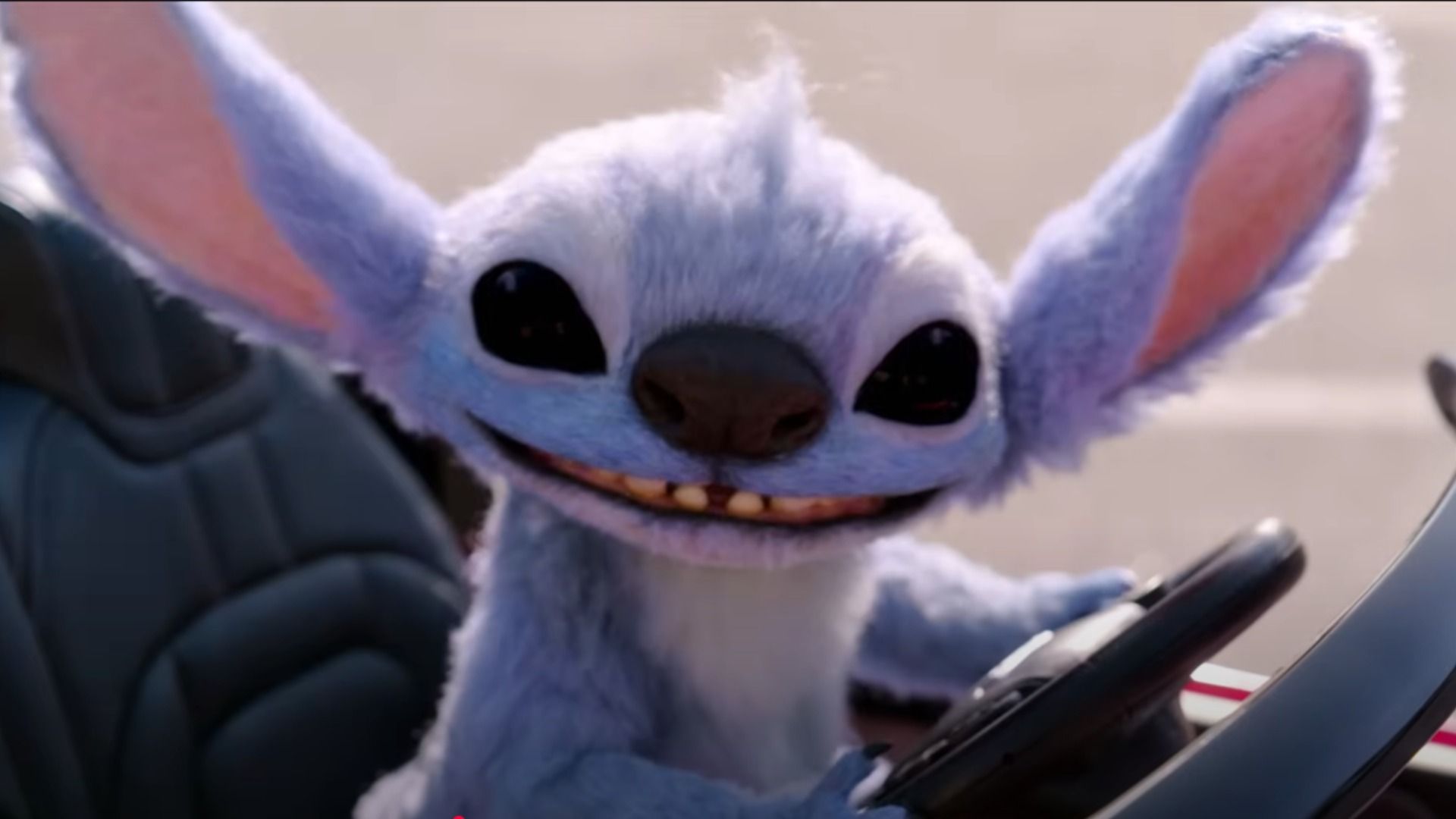Blue alien Stitch sits behind the wheel of a small car and smiles