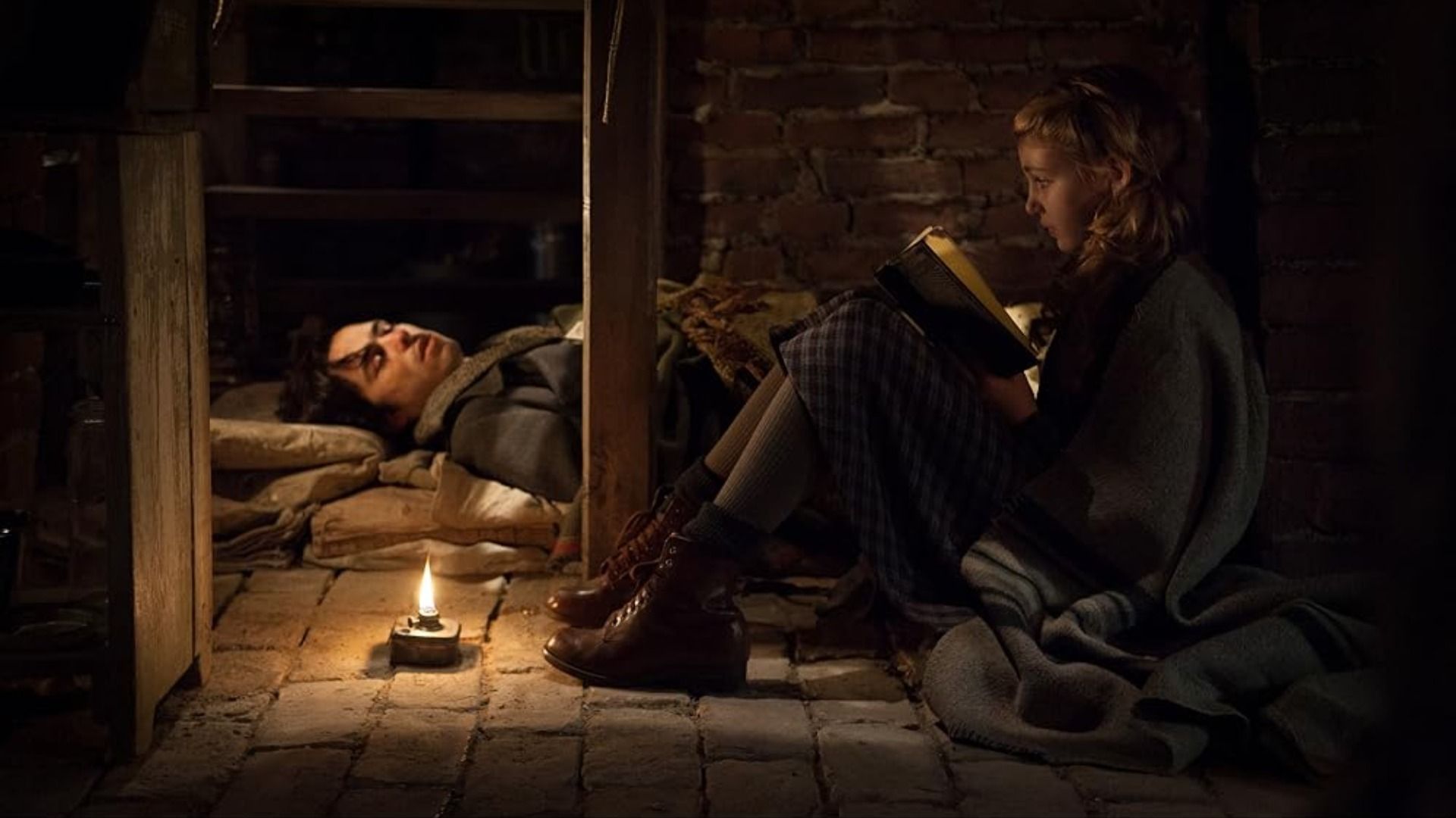 Actress Sophie Nélisse sits in a basement with a book in her hands near a man sleeping on the floor