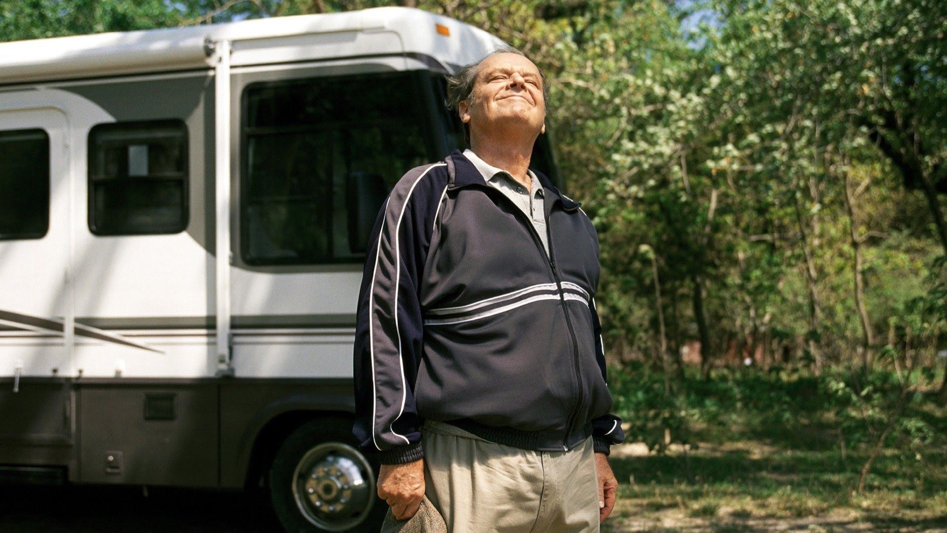 Jack Nicholson in a tracksuit stands in front of an RV enjoying a sunny day surrounded by trees