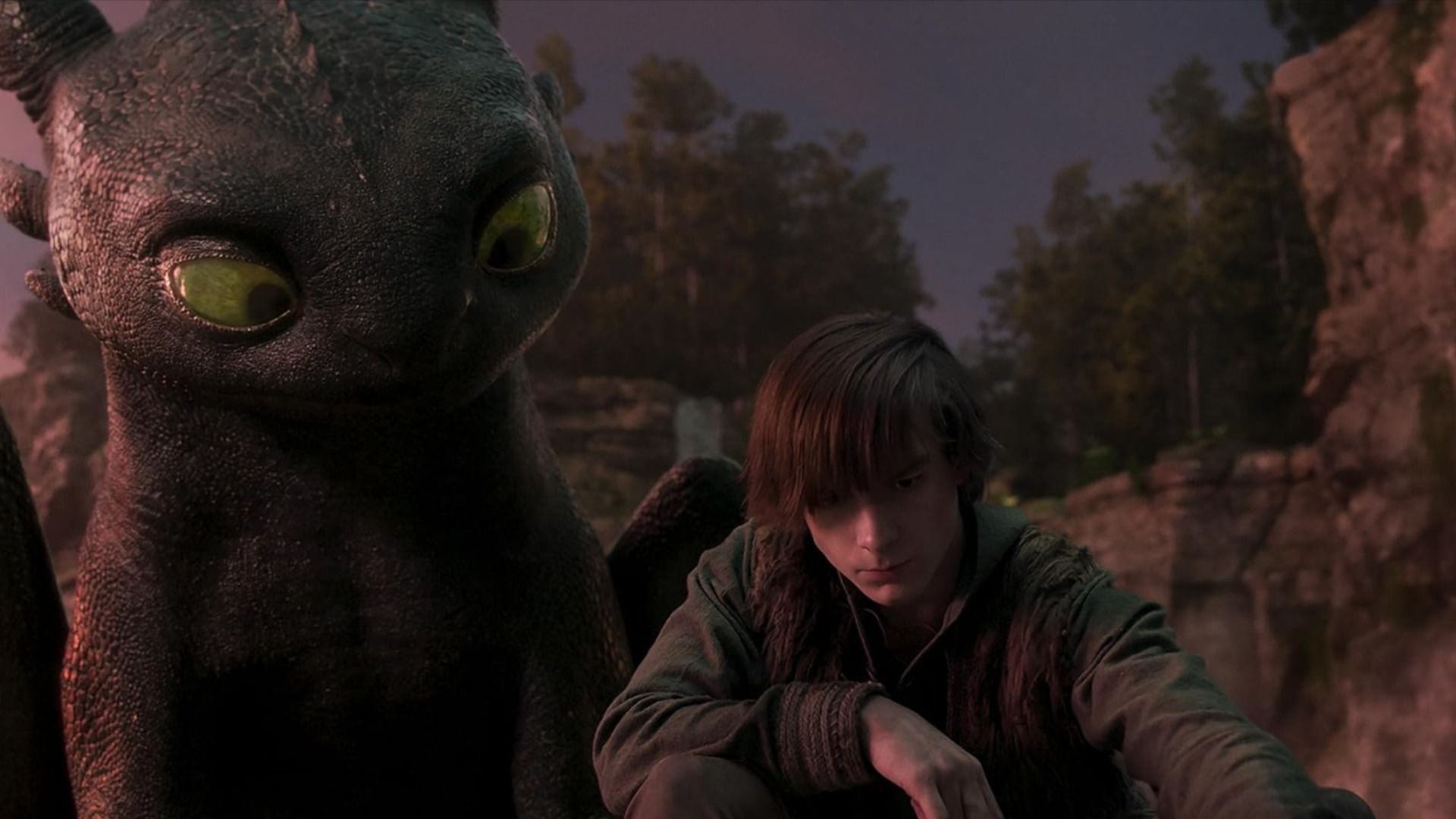 A boy in gray clothing sits next to a black dragon with green eyes