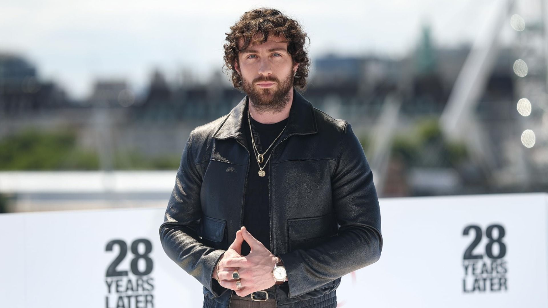 Actor Aaron Taylor-Johnson in a black leather jacket stands against a blurred city background