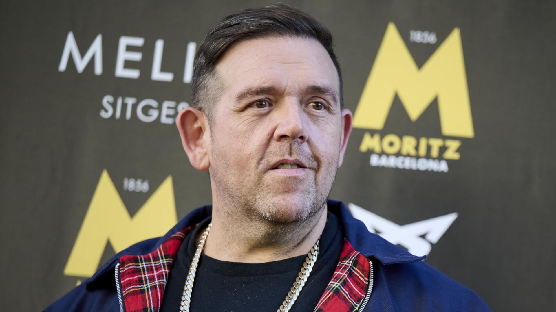Actor Nick Frost in a blue jacket with a gold chain around his neck smiles against a backdrop display