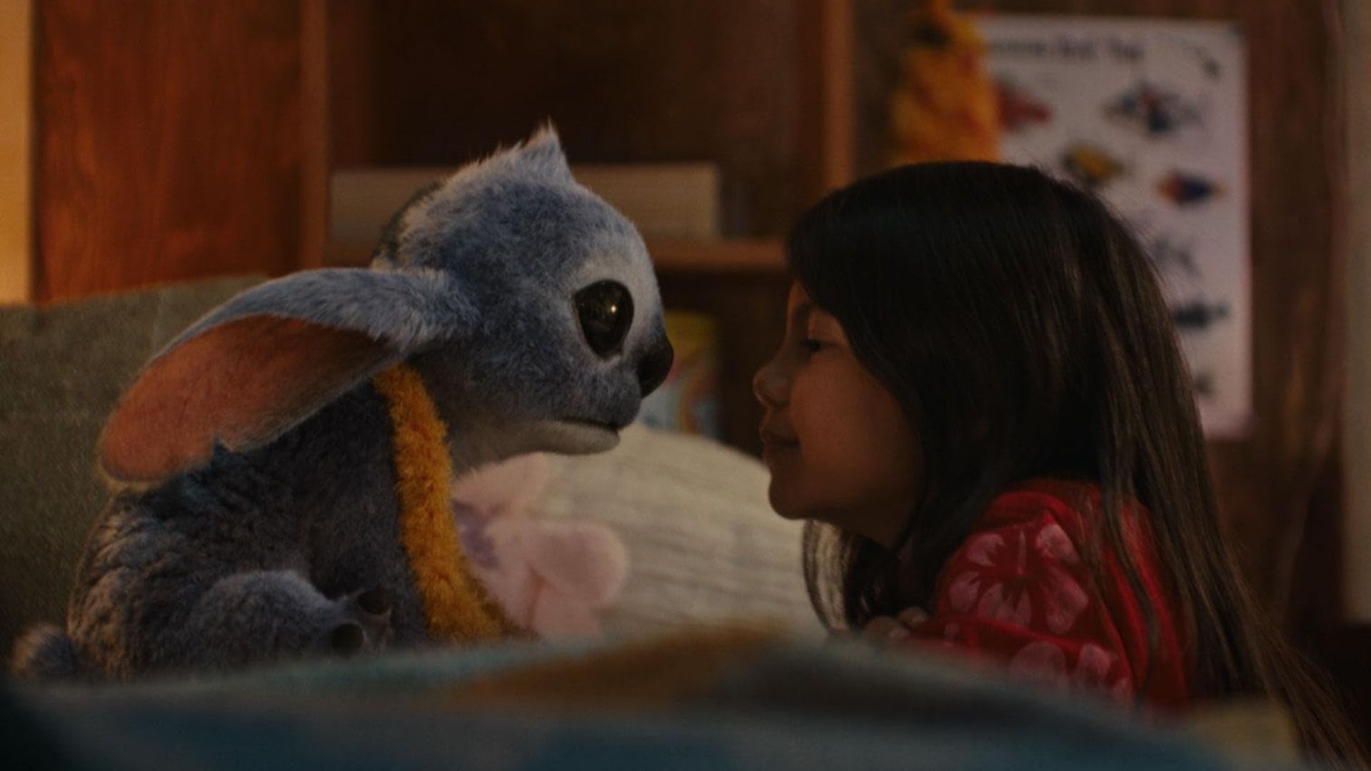Blue creature with large ears and a girl in a red dress looking at each other