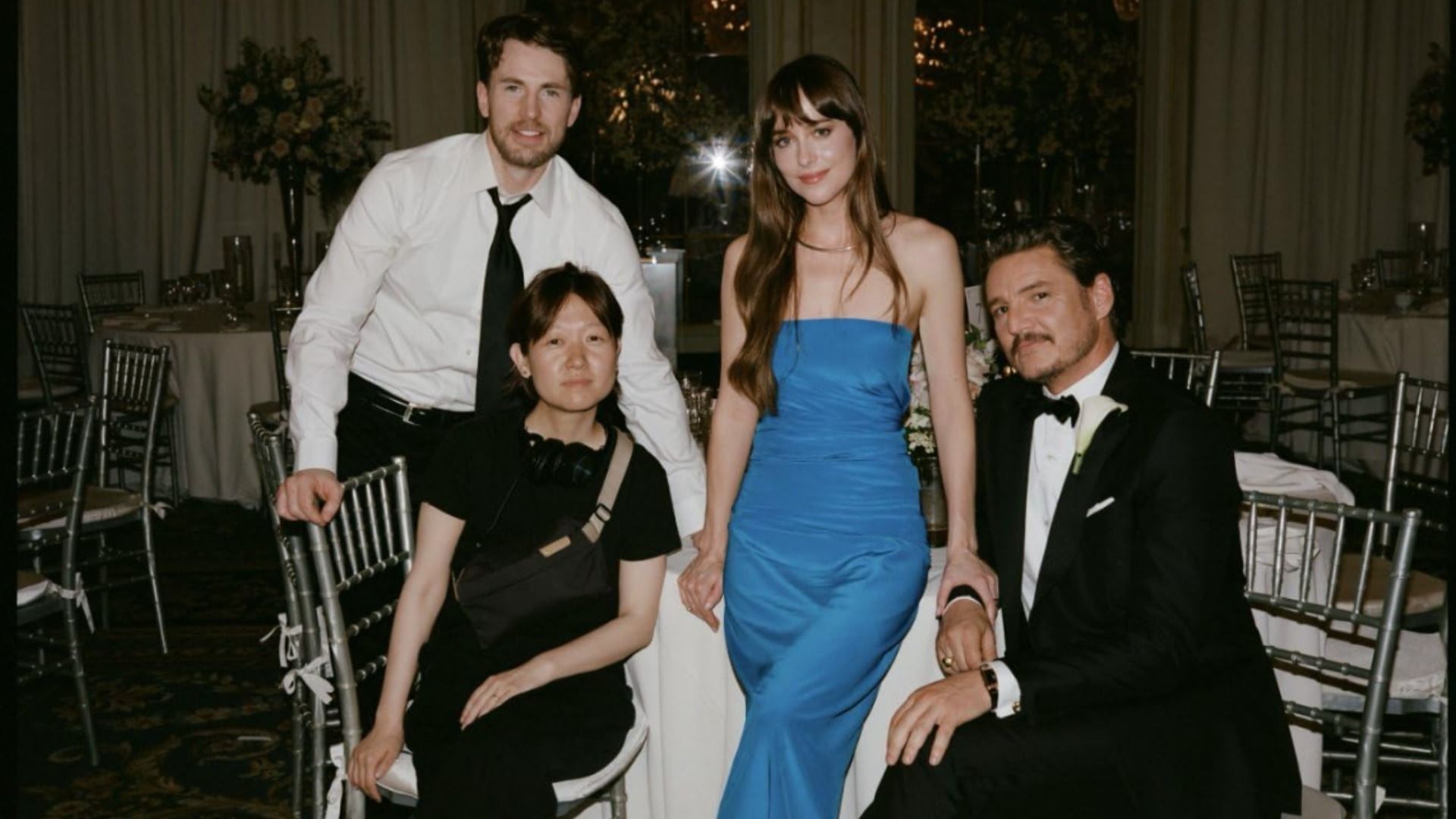 Actors Dakota Johnson, Chris Evans and Pedro Pascal sitting in evening wear at a white table