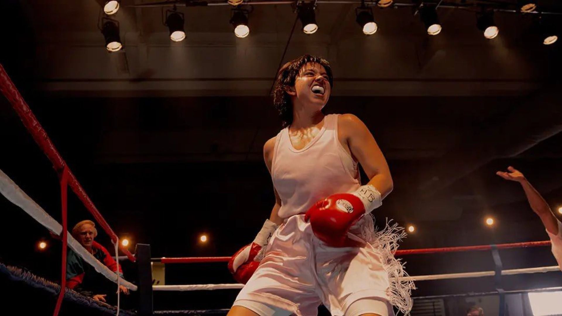 Actress Sydney Sweeney in a white tank top and red gloves stands on a boxing ring