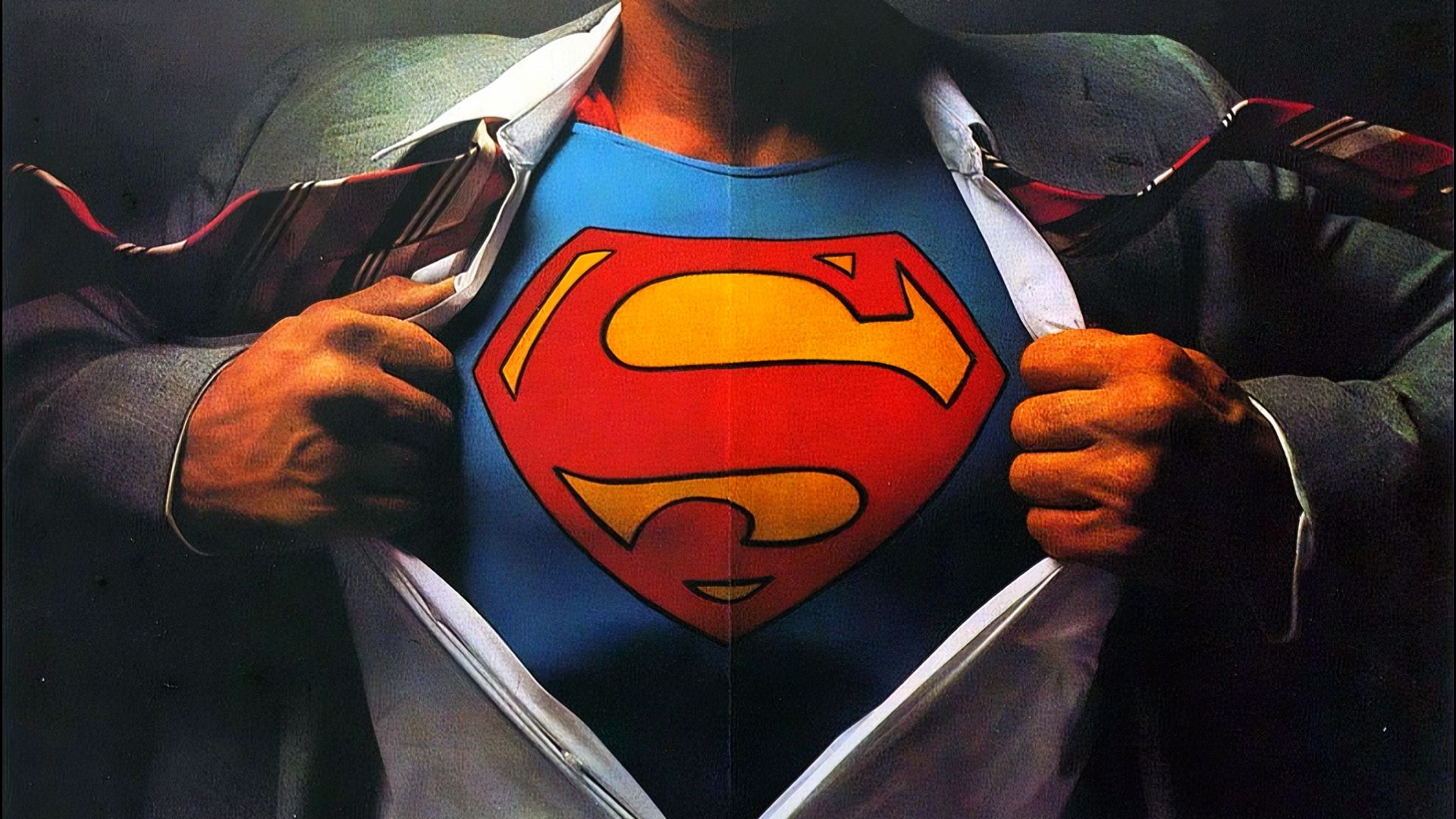 A man unbuttoned his shirt and reveals a superhero costume with the letter S on his chest