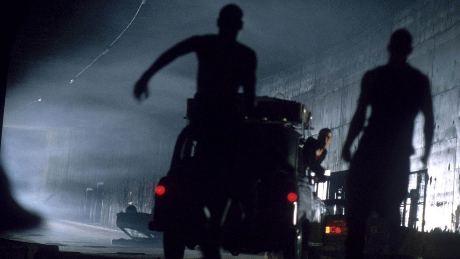 Actor Cillian Murphy standing by a car while zombies run toward him
