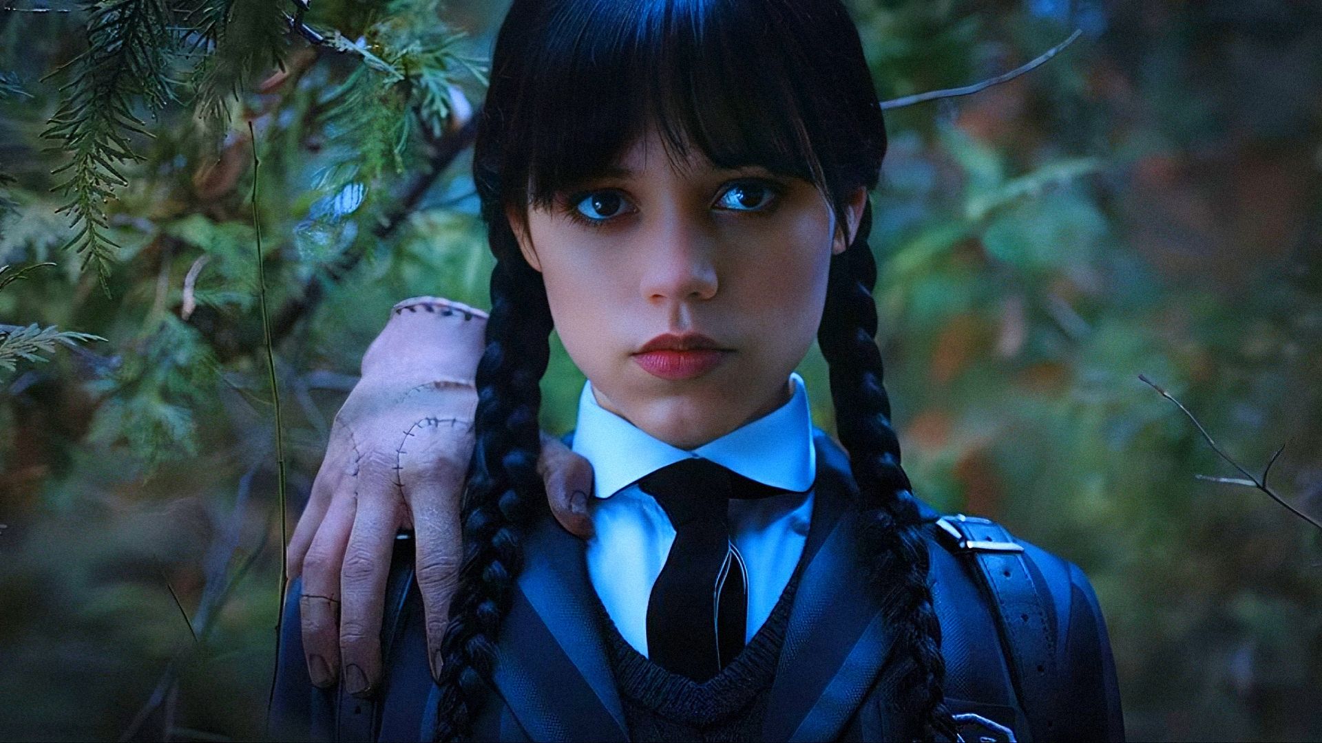 Actress Jenna Ortega in school uniform with a hand on her shoulder looks at the camera
