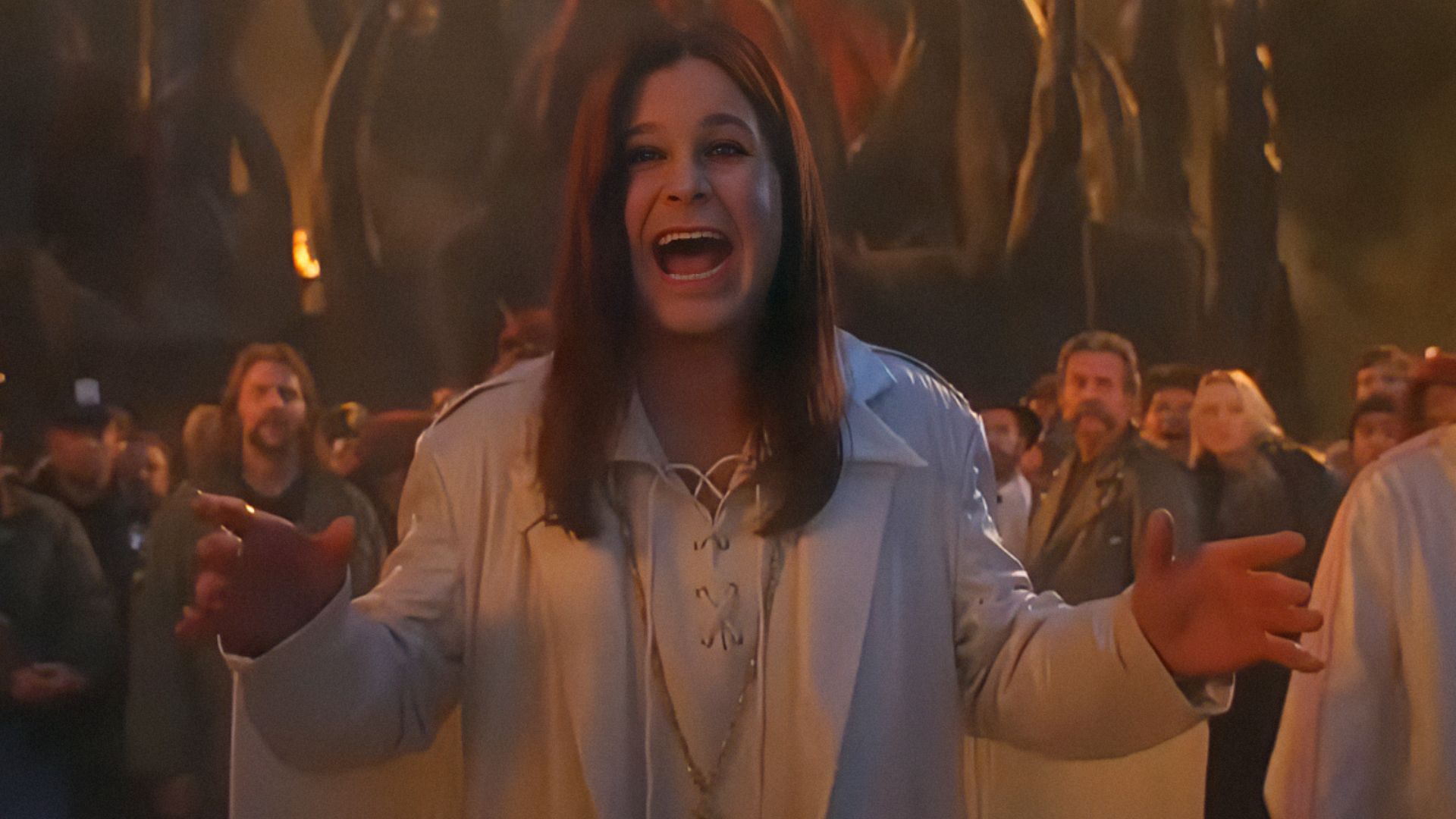 Singer Ozzy Osbourne in a white jacket spreads his arms wide and smiles