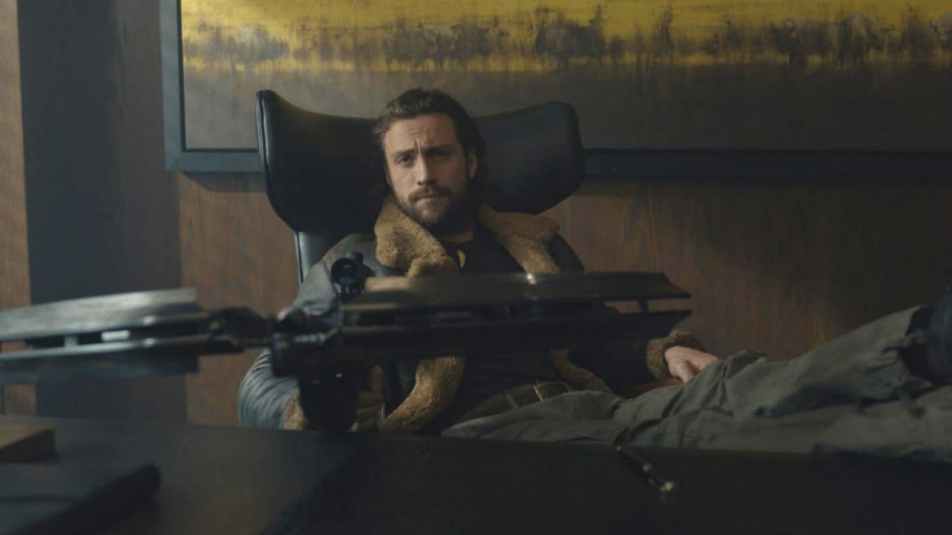 Actor Aaron Taylor-Johnson sits at a table with a crossbow in his hands