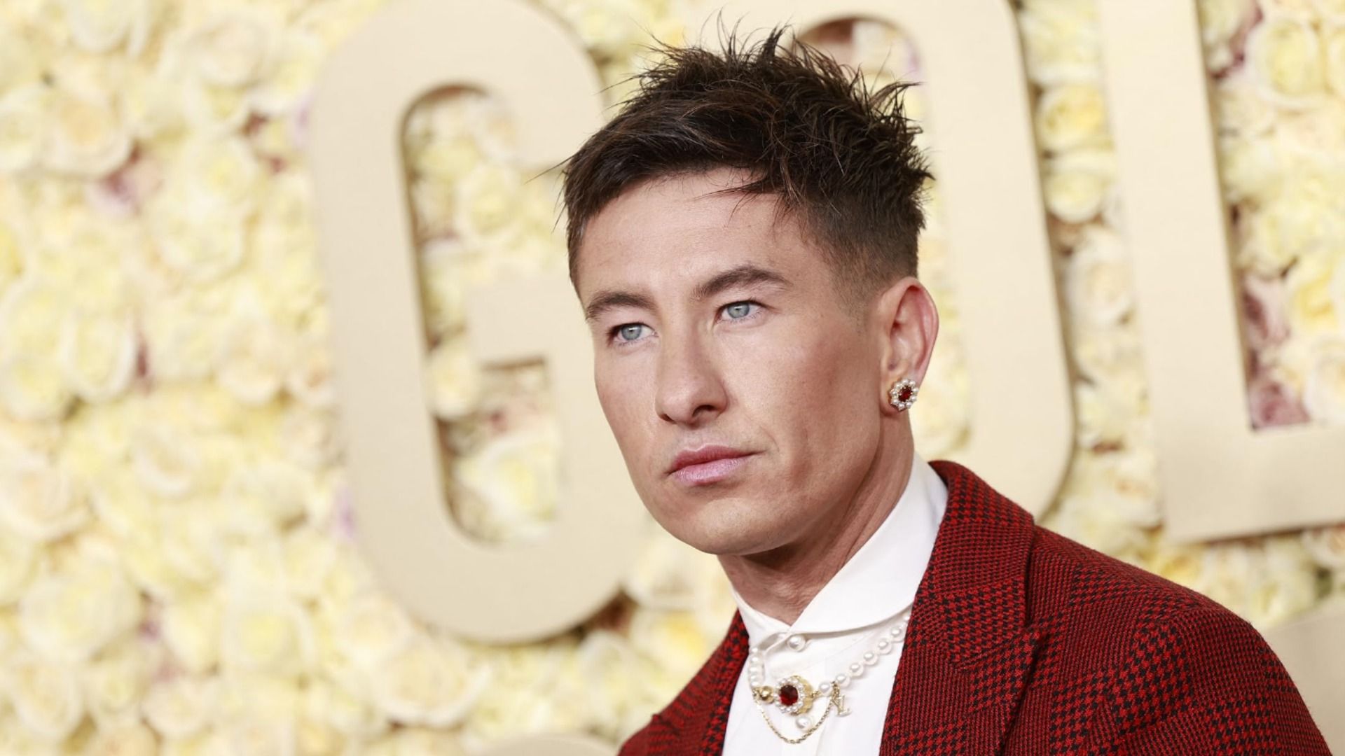 Actor Barry Keoghan in a red jacket with an earring standing against a yellow background