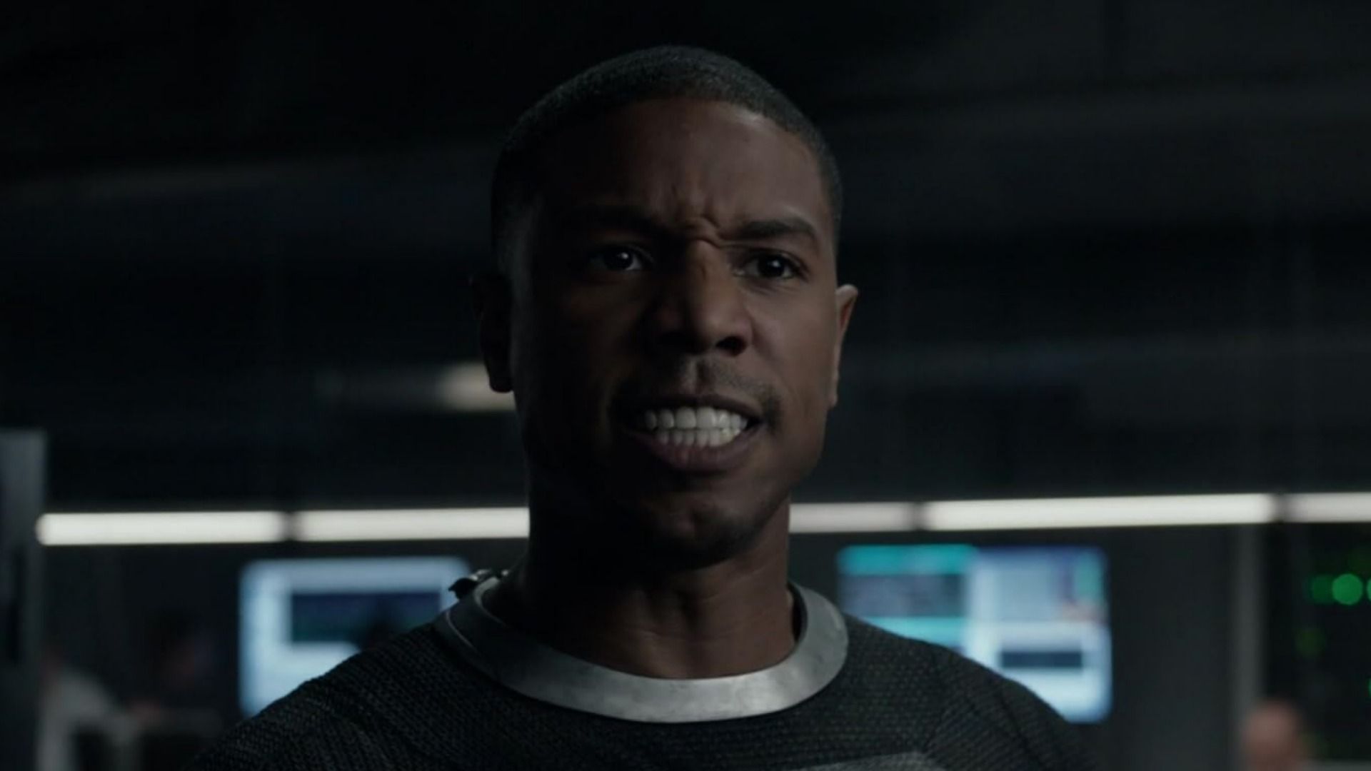 Actor Michael B. Jordan in a gray suit looking angry against a blurred background