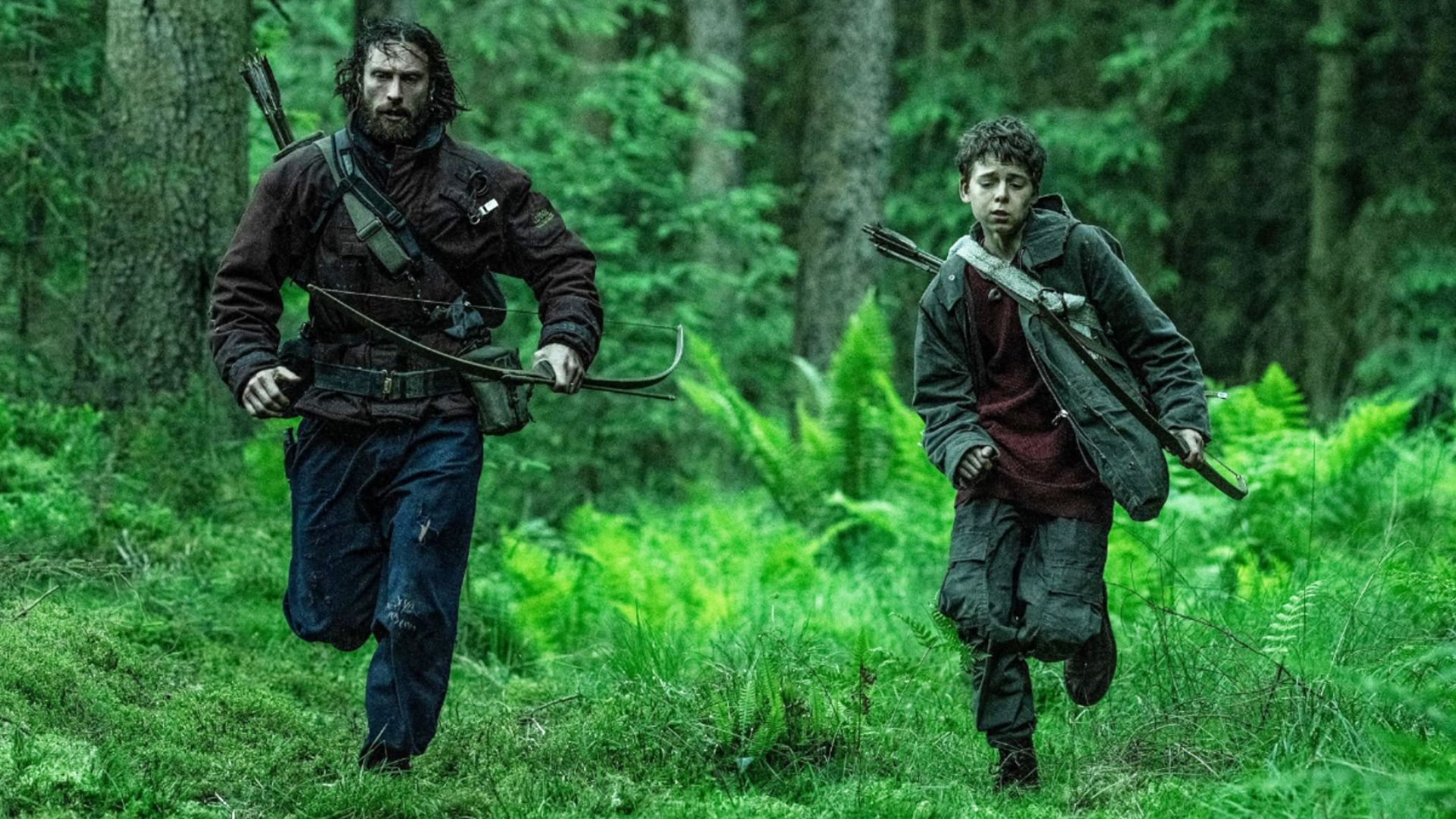 Actor Aaron Taylor-Johnson in dirty clothes runs through the forest alongside a child with a bow