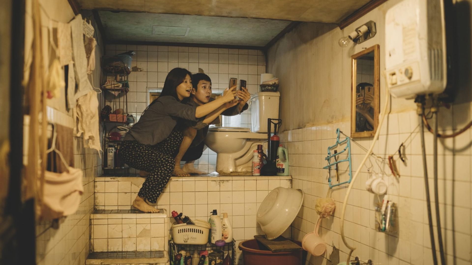A guy and girl in loungewear sitting next to a toilet with phones in their hands