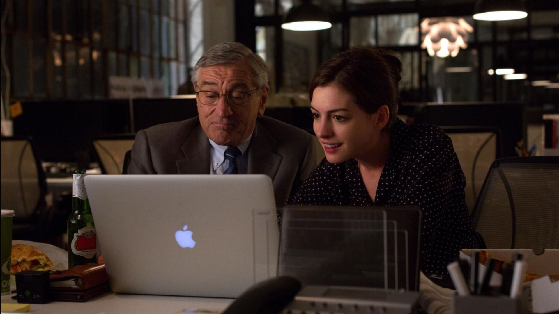 Actor Robert De Niro in a gray suit jacket and actress Anne Hathaway in a black dress sitting at a table
