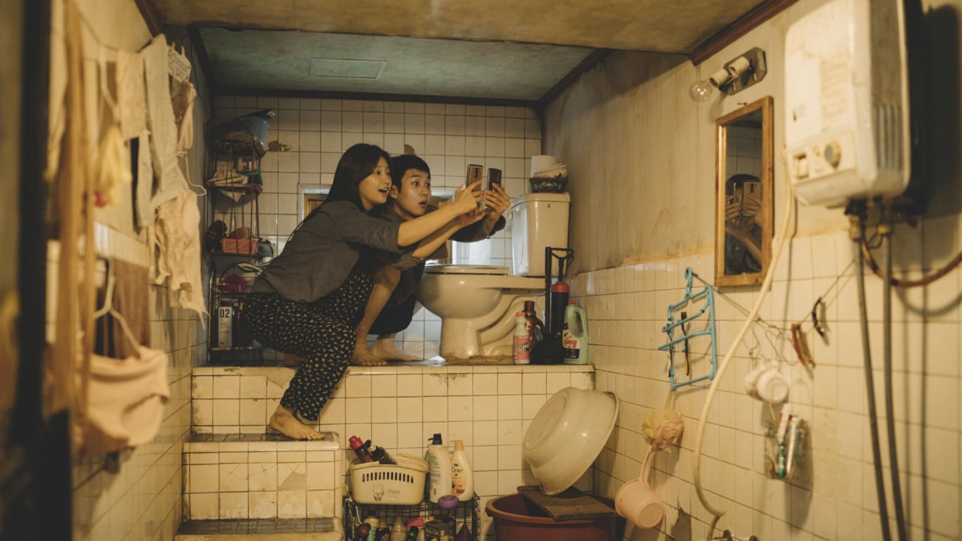 A guy and girl are sitting by the toilet with phones in their hands