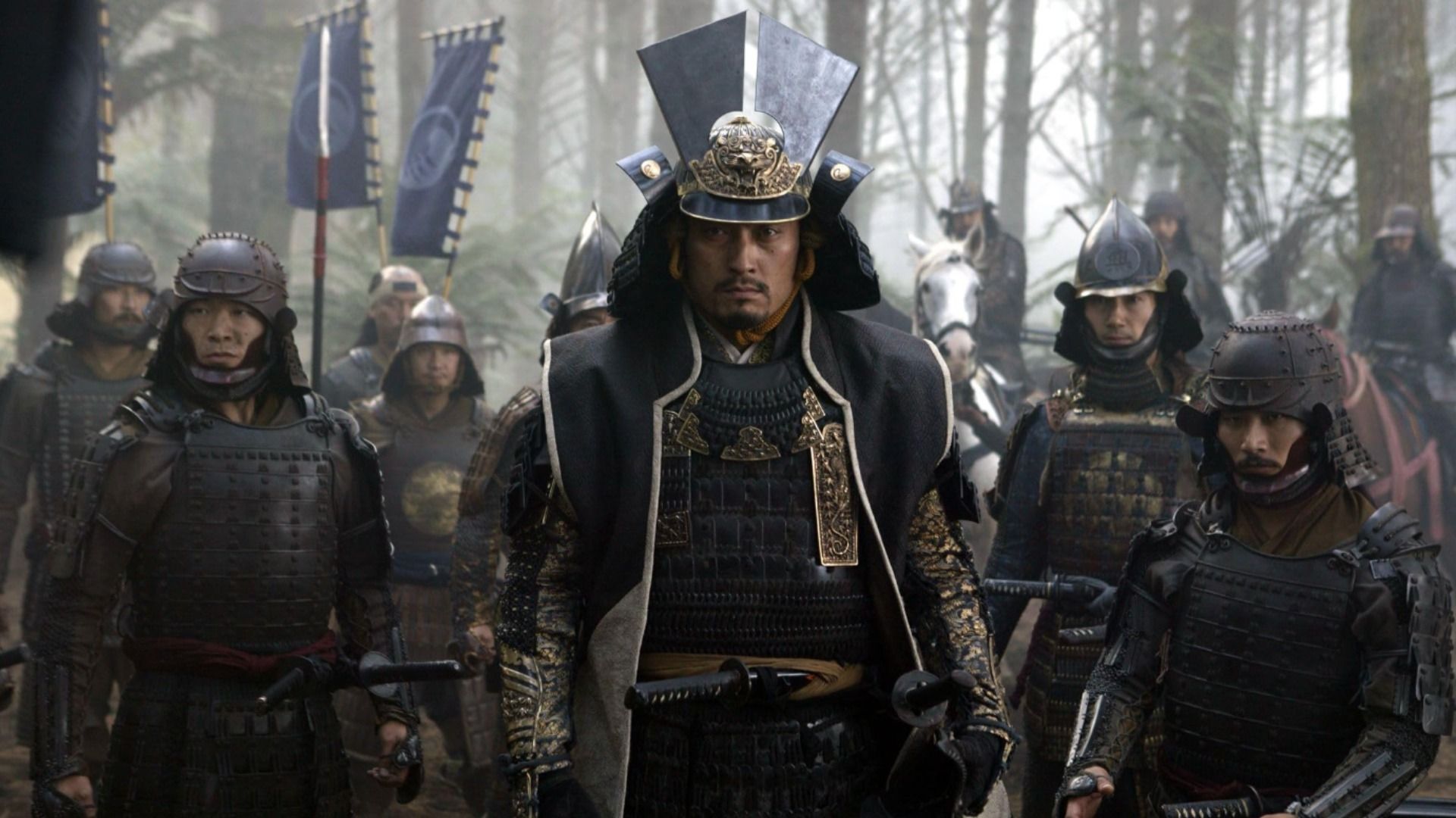 Actor Ken Watanabe in dark samurai armor stands surrounded by other samurai