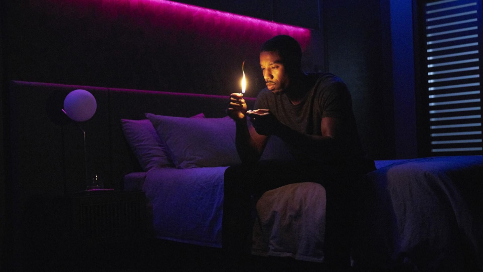 Actor Michael B. Jordan sits on a bed with a match in his hands