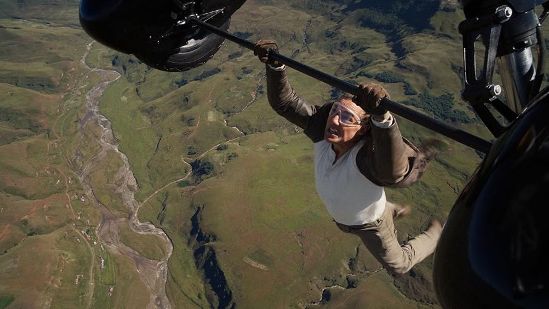 Actor Tom Cruise in a brown jacket grips the wheels of a flying plane