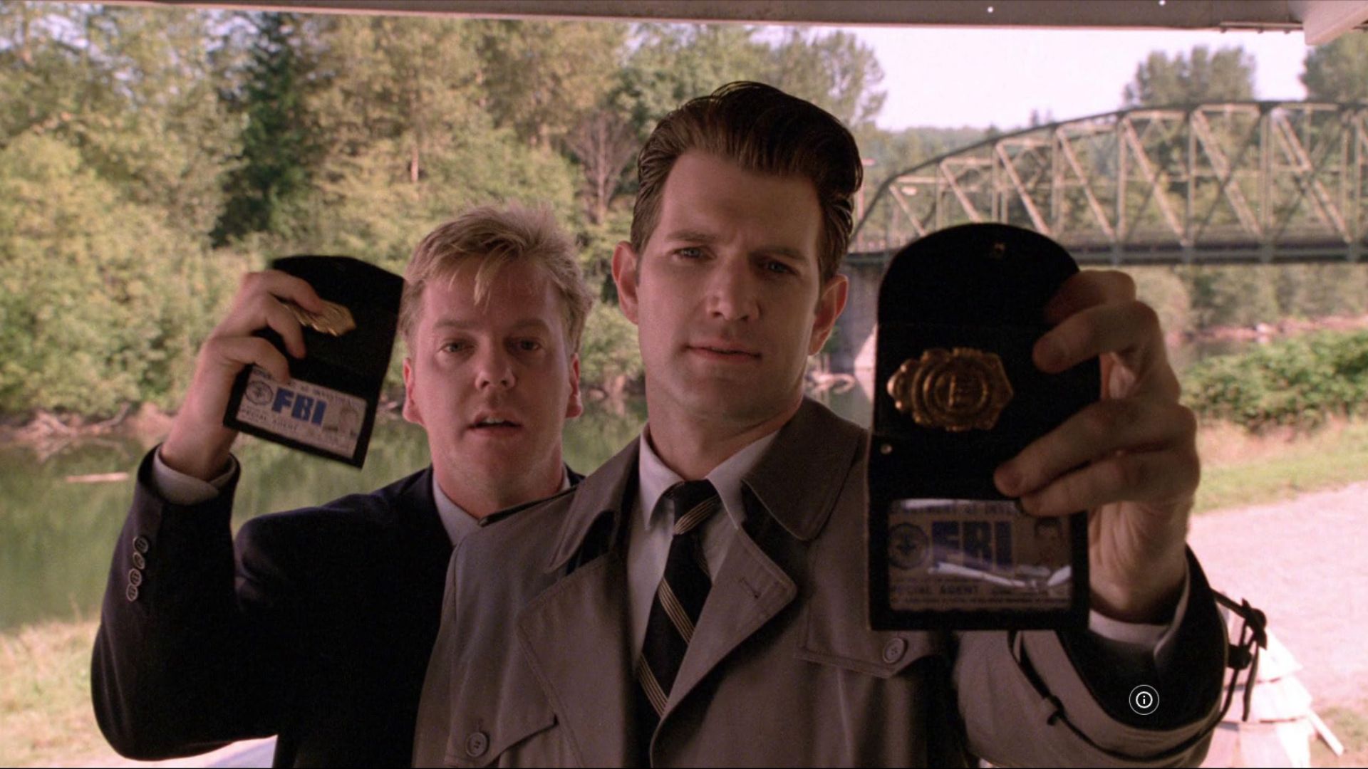 Two male police officers in black and beige coats holding police badges in their hands
