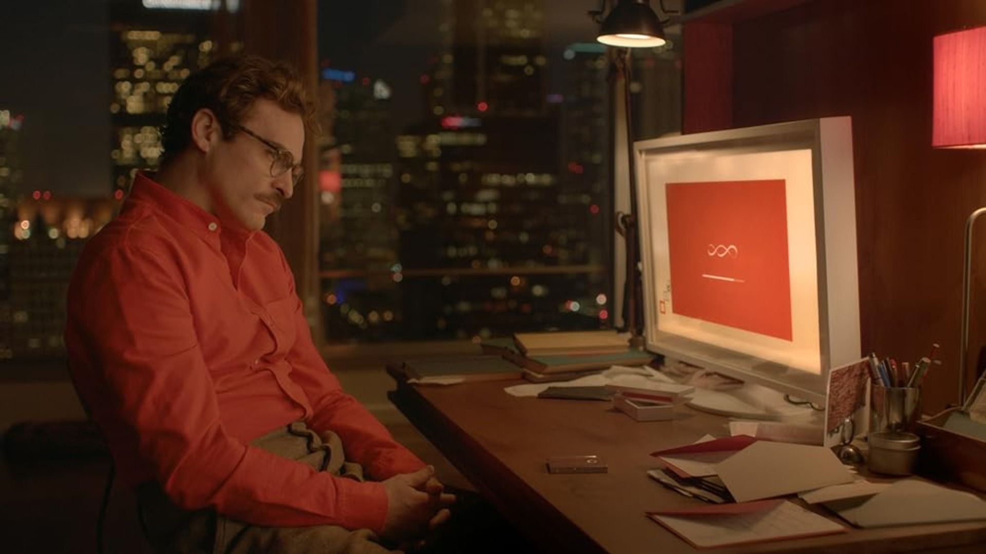 Actor Joaquin Phoenix in a red shirt sits at a table with a computer on it