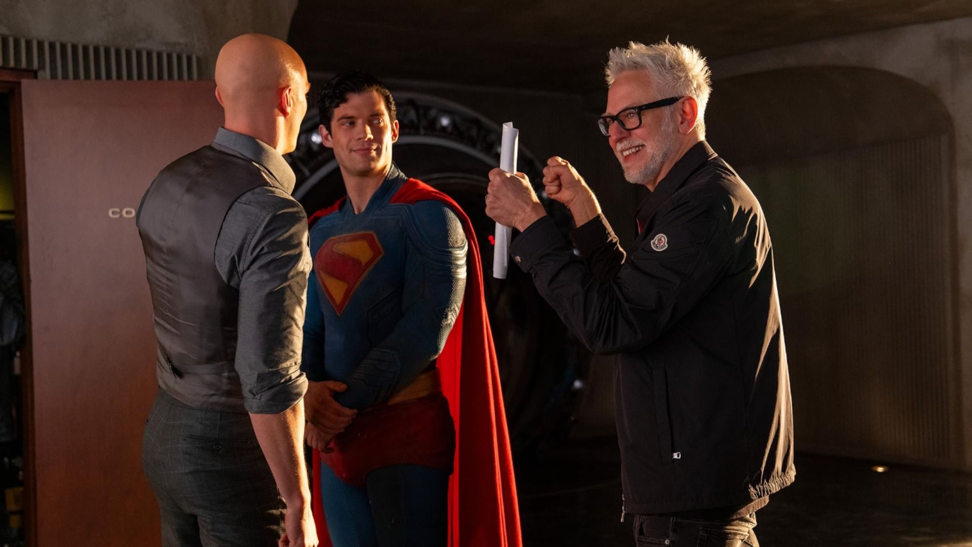Director James Gunn holding papers talks with actor David Corenswet in Superman costume and with Nicholas Hoult who is bald