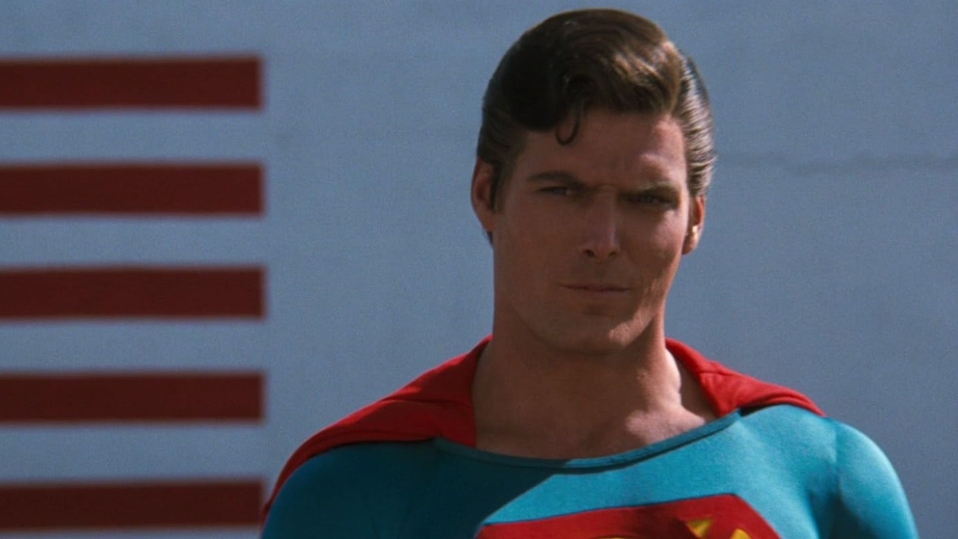 Actor Christopher Reeve in the blue and red Superman costume glares menacingly to the side