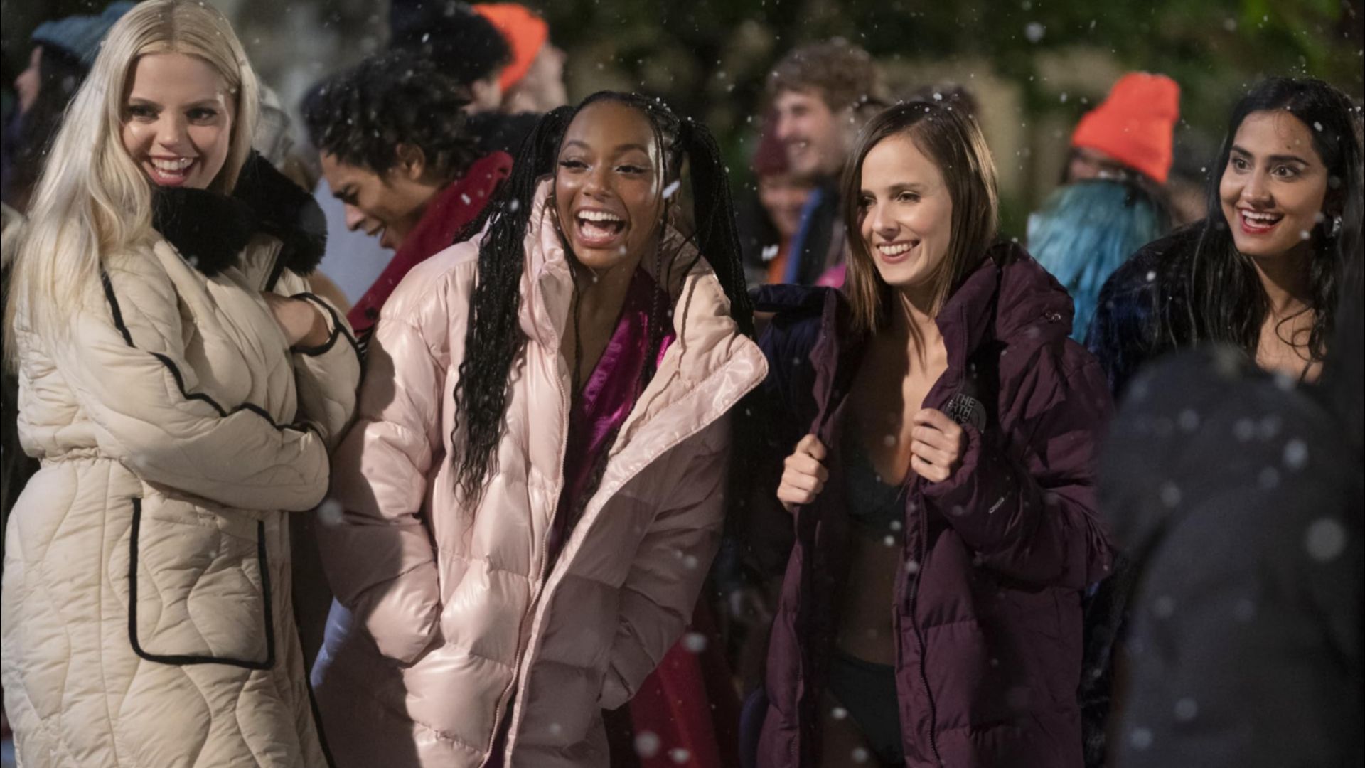 Four girls stand in colorful jackets against a backdrop of falling snowflakes