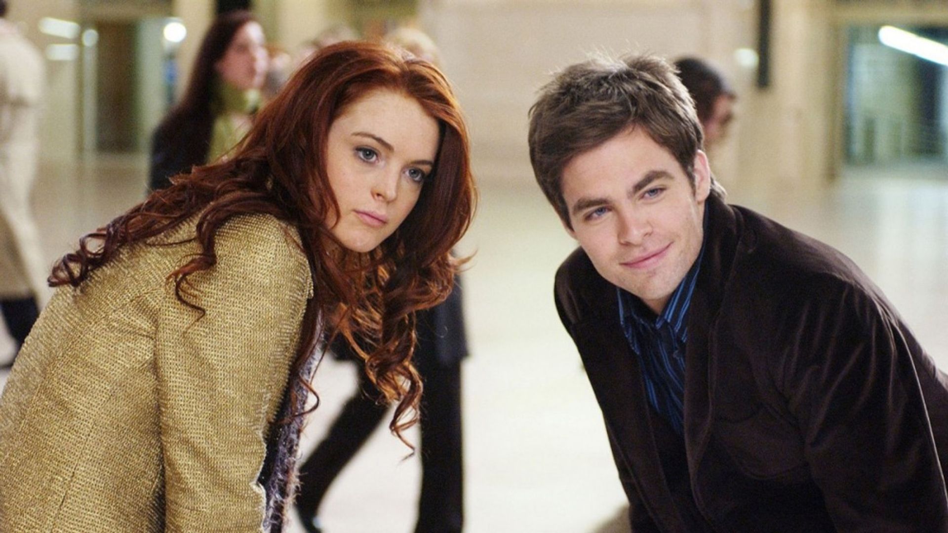Lindsay Lohan and Chris Pine stand side by side, leaning forward in a crowded room