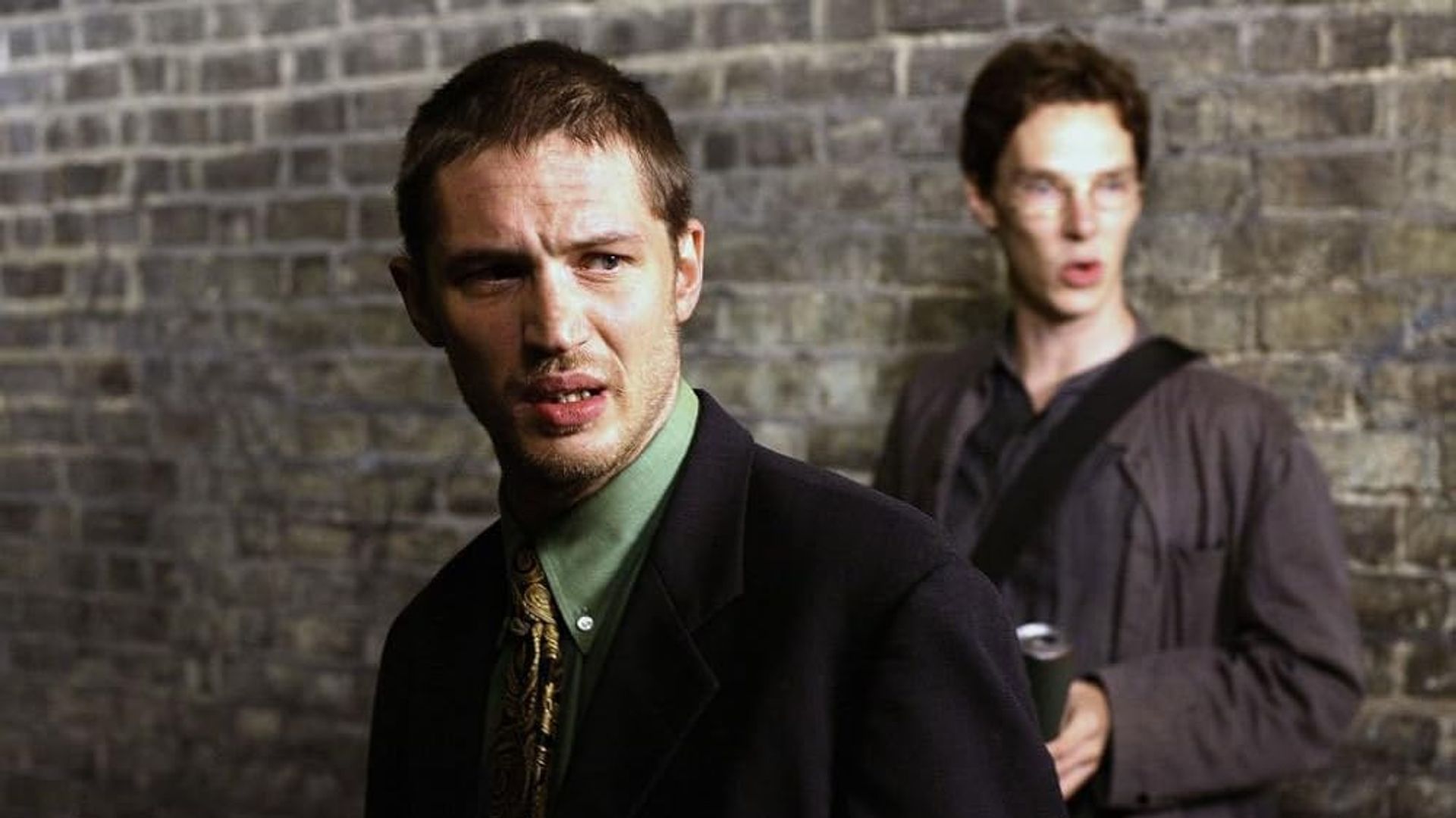 Young Tom Hardy and Benedict Cumberbatch standing against a brick wall