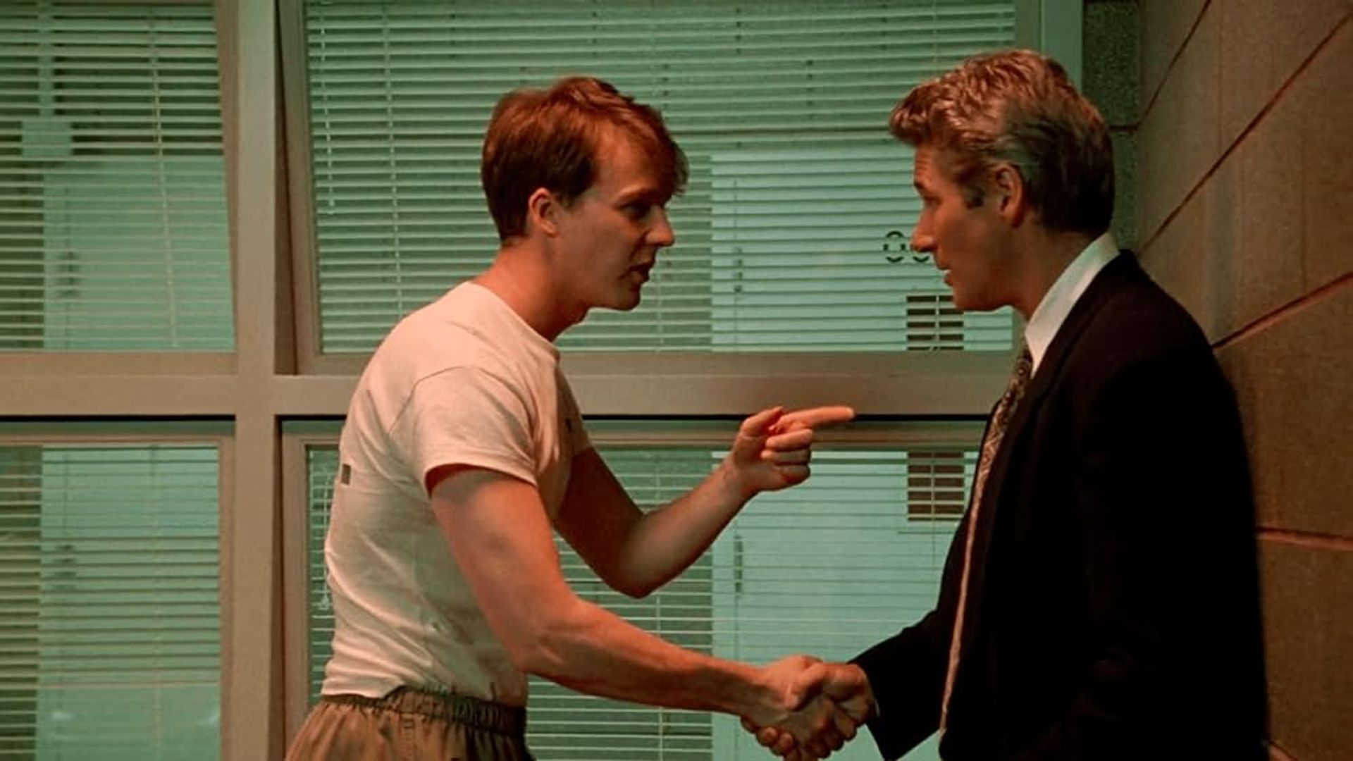 Edward Norton in a t-shirt shaking hands with Richard Gere in a suit, pointing at him with his finger