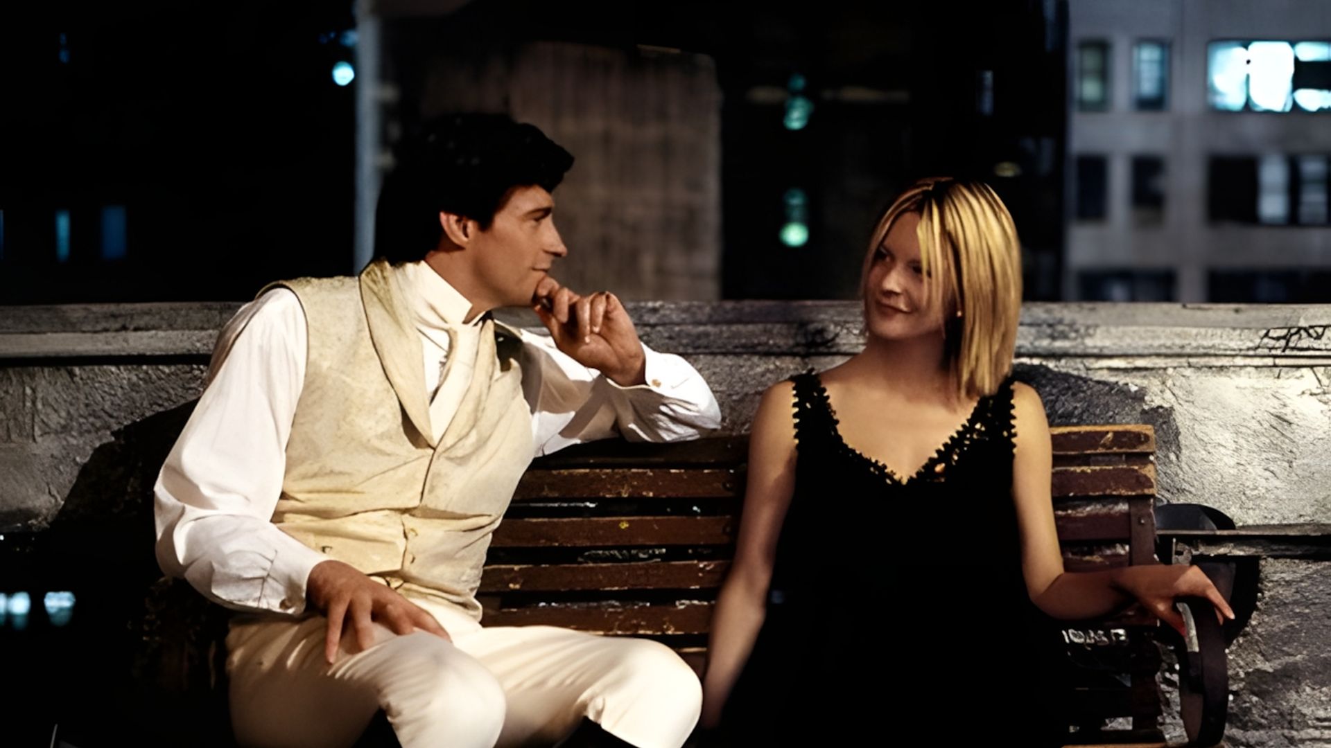 Hugh Jackman and Meg Ryan sitting on a bench at night with the city in the background