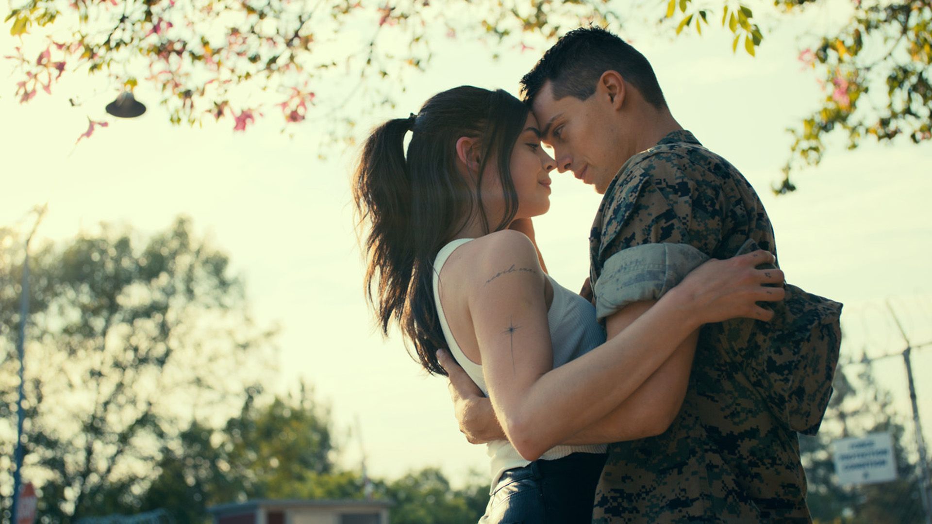 Sofia Carson and Nicholas Galitzine embrace while standing under a tree