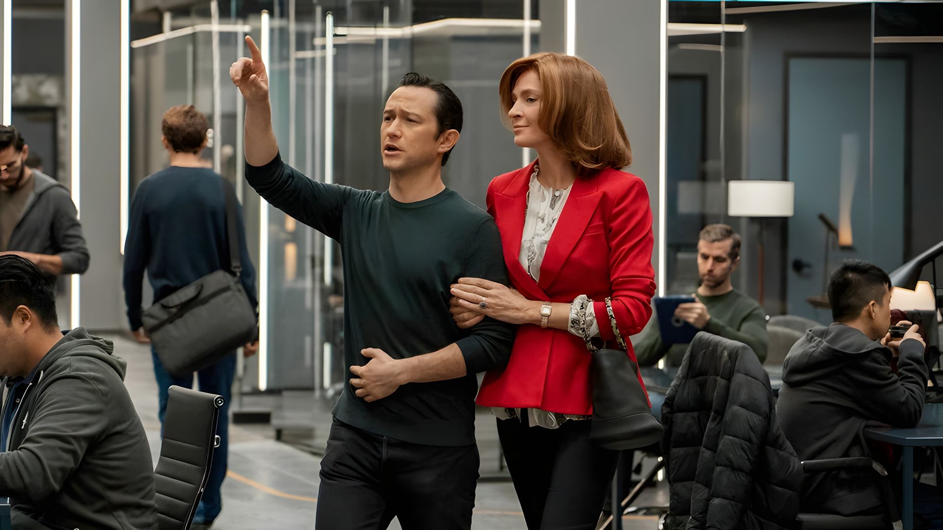 Joseph Gordon-Levitt in dark clothing points forward while Uma Thurman in a red jacket holds onto his arm