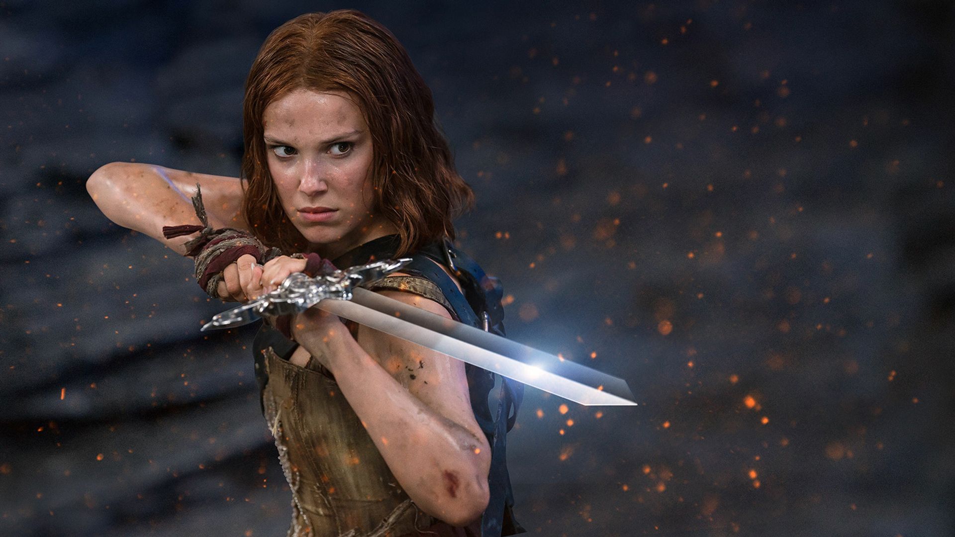 Millie Bobby Brown with red hair in battle attire holds a sword, preparing to attack against a backdrop of sparks and dark sky