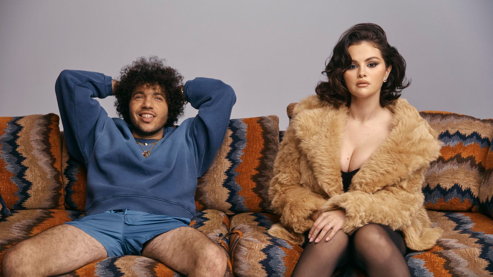 Selena Gomez in a fur coat and Benny Blanco in a blue sweatshirt and shorts sitting relaxed