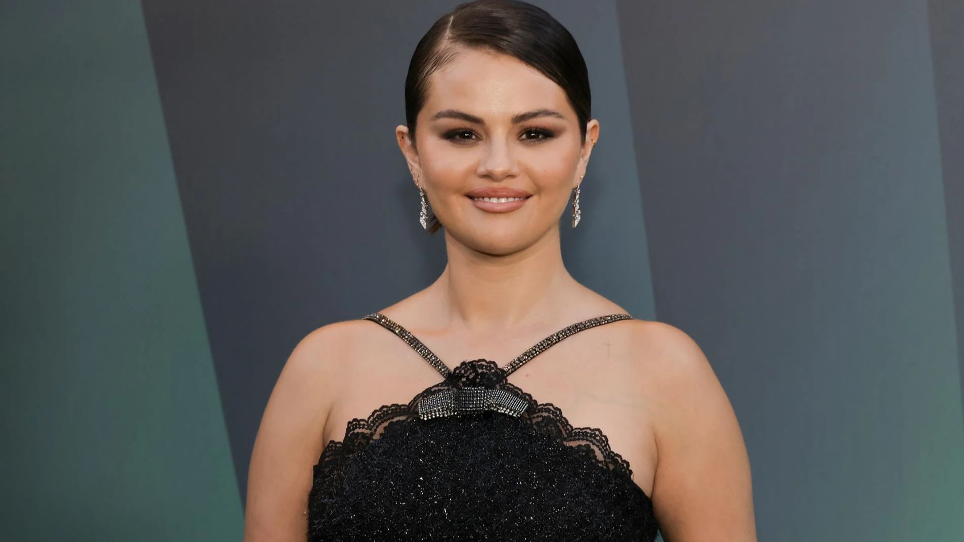 Selena Gomez in a black dress poses for cameras with a gentle smile