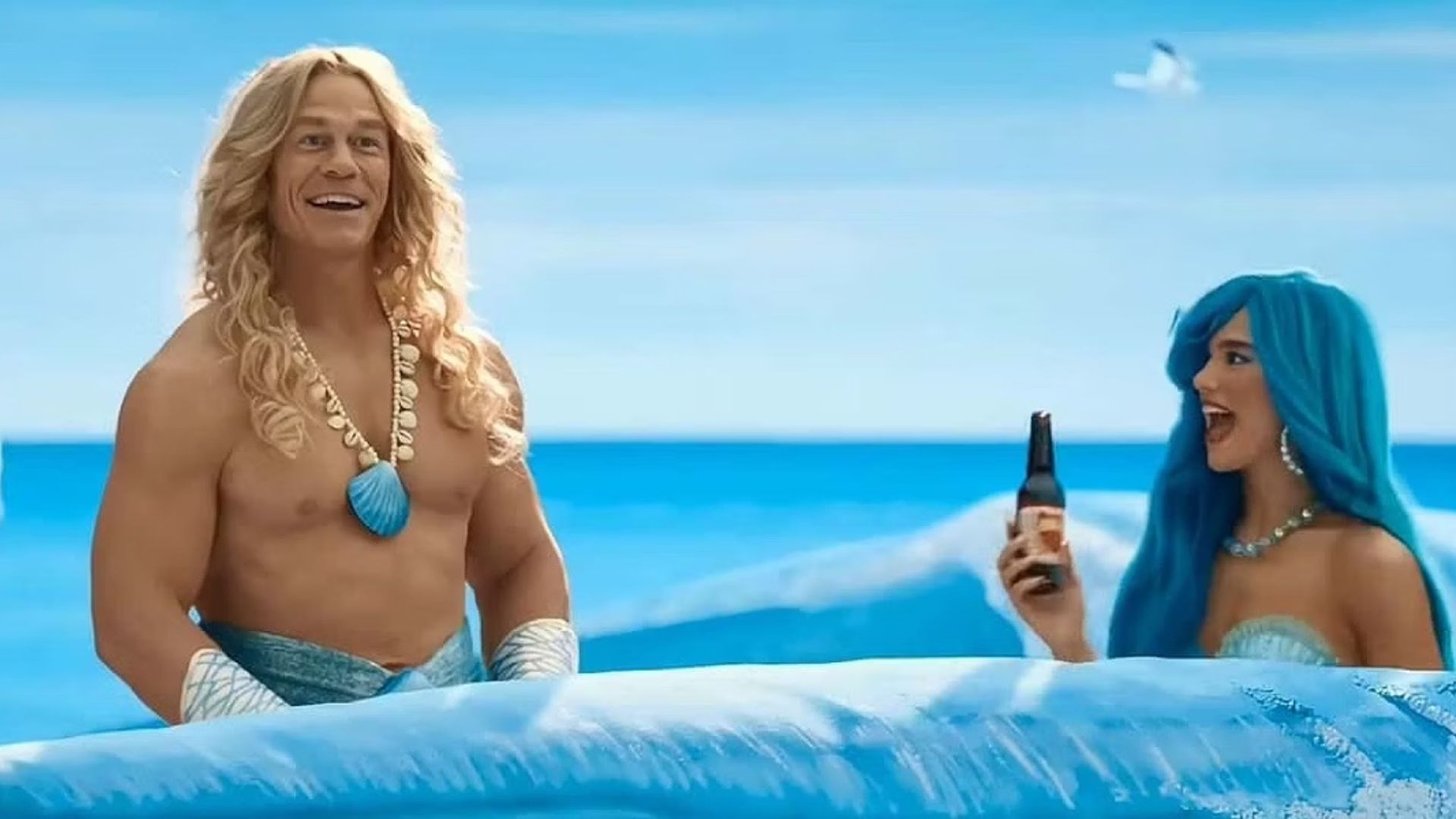 John Cena and Dua Lipa in mermaid costumes swimming through painted waves