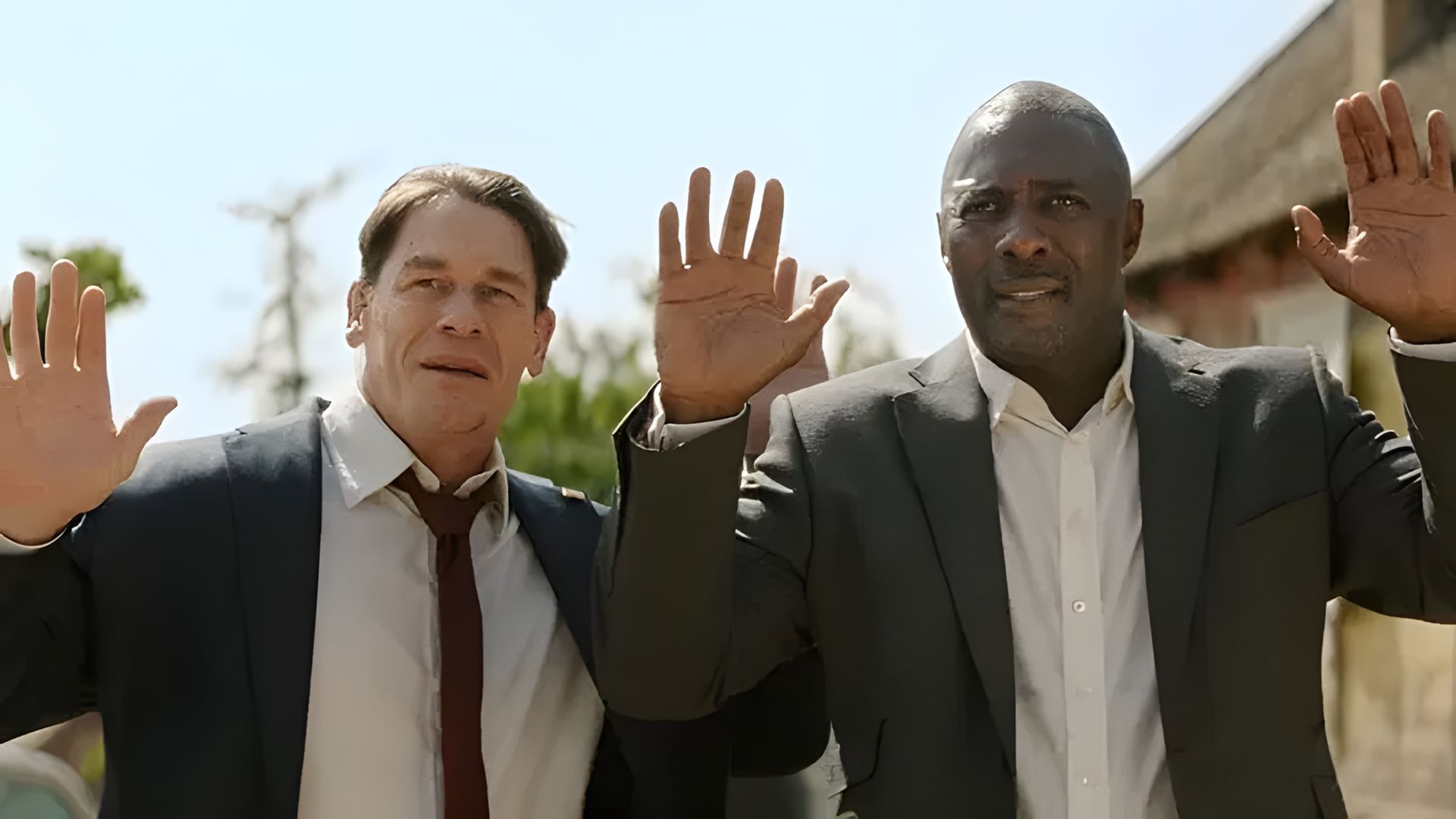 John Cena and Idris Elba in suits raising their hands up, scene from an action movie