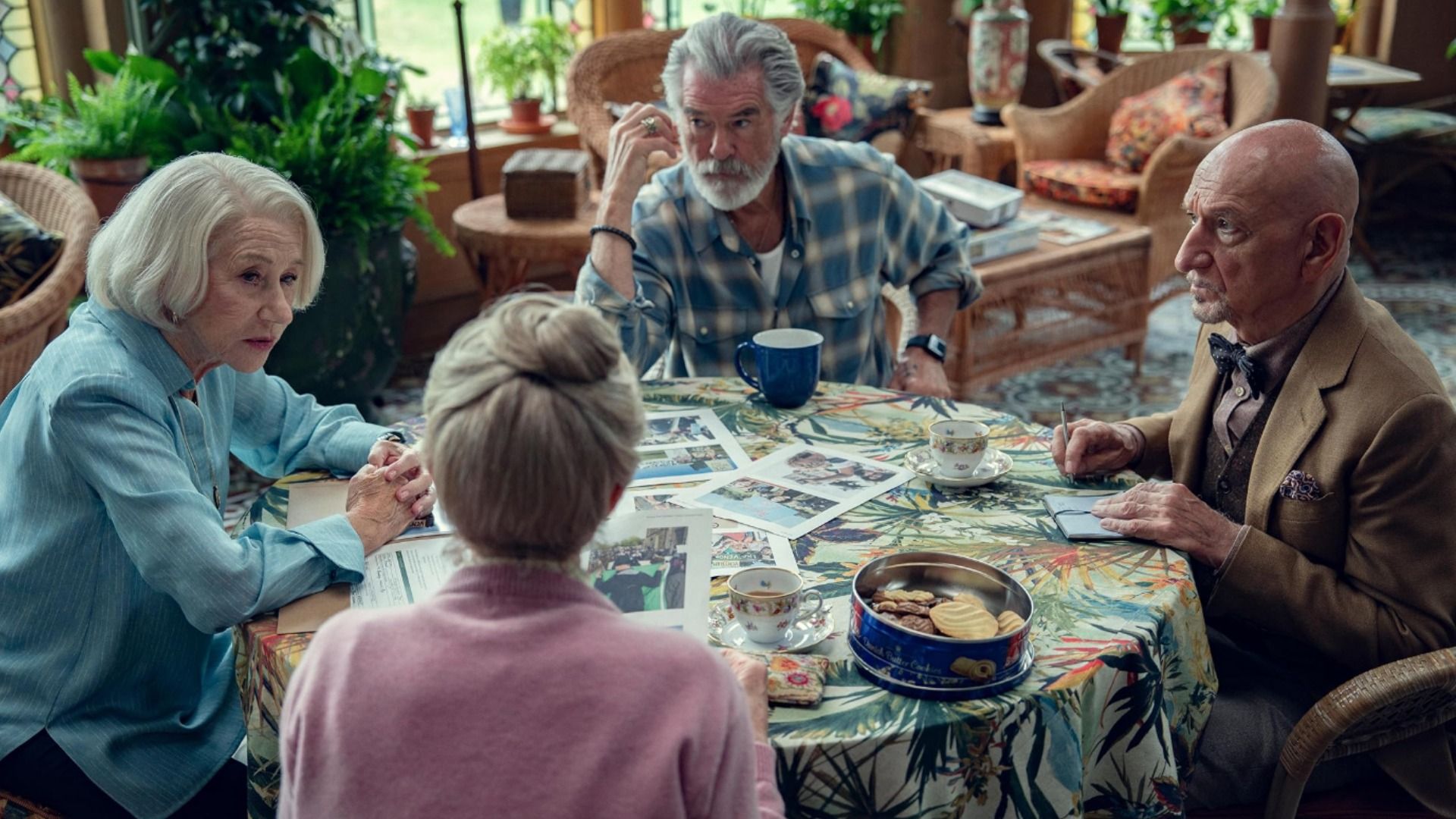Two elderly men and two elderly women are sitting at a table with a pile of photographs