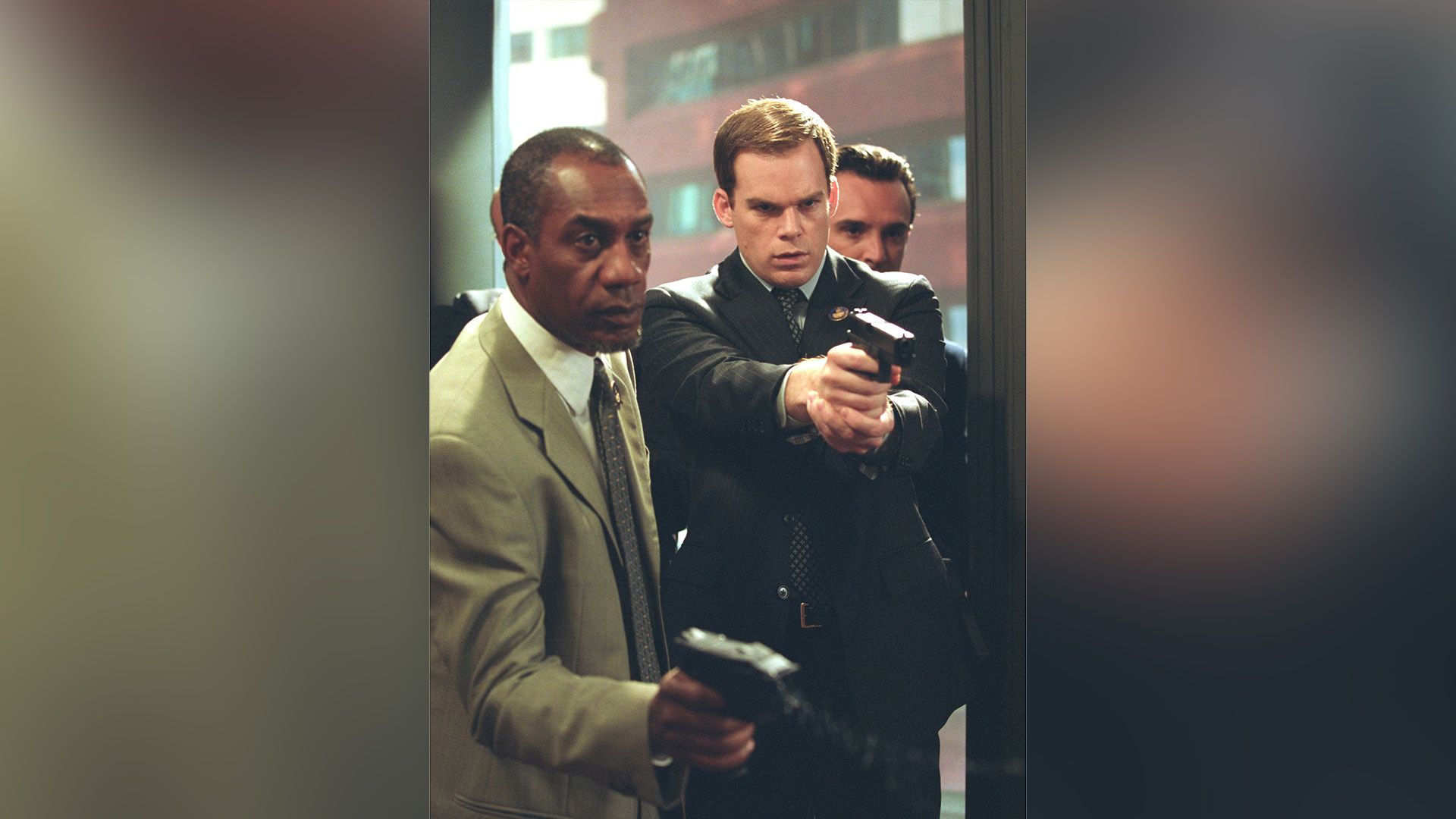 Michael C. Hall and a Black man standing with arms extended holding weapons