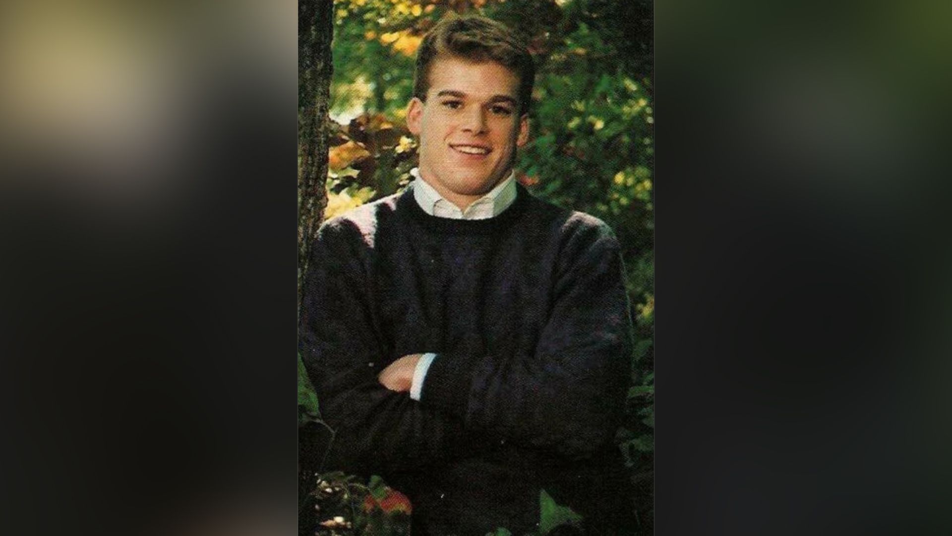 Young Michael C. Hall stands with his arms crossed over his chest, grinning widely