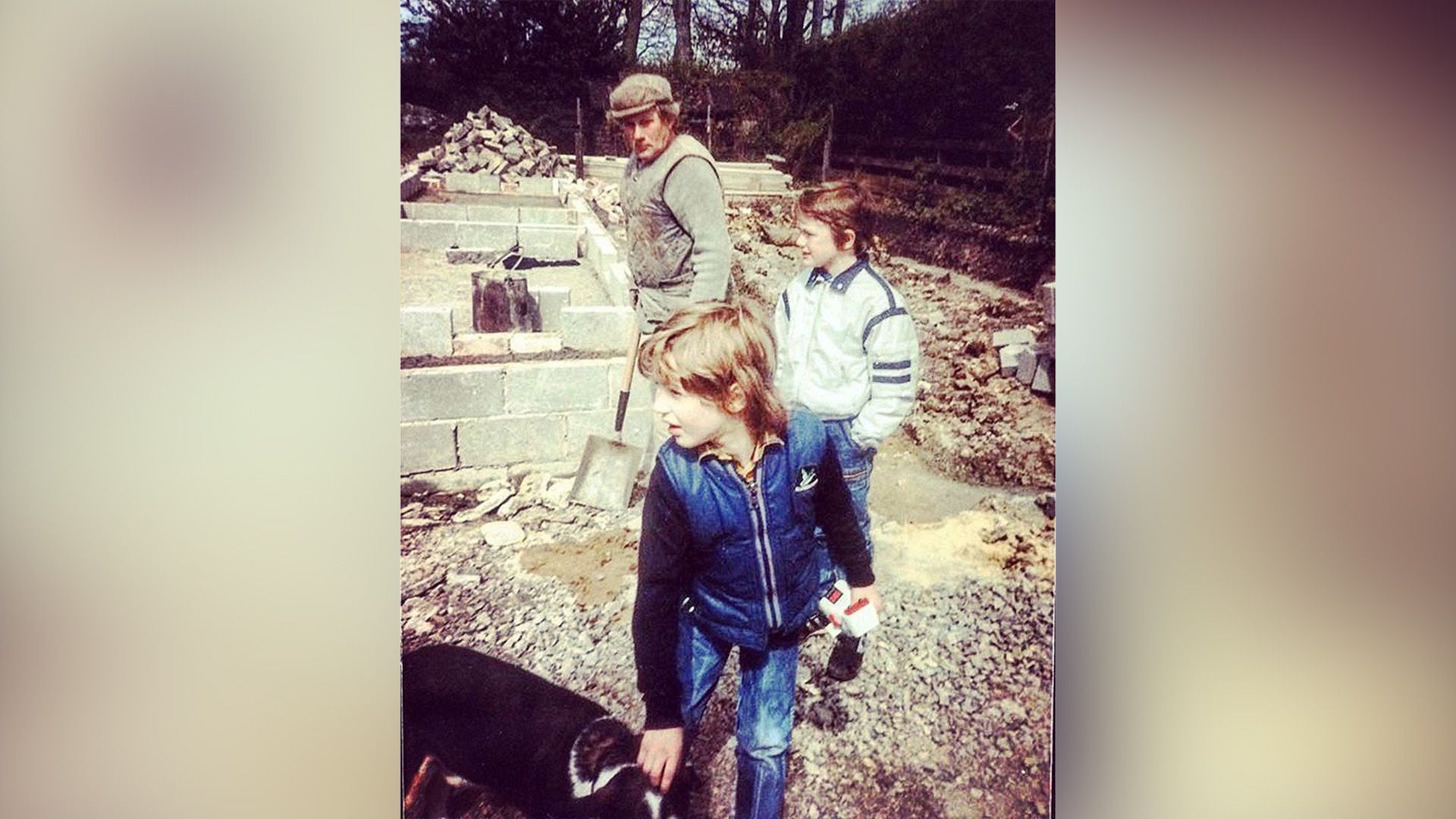 Little Tom Hardy pets a dog in the yard with his cousin and grandfather standing nearby