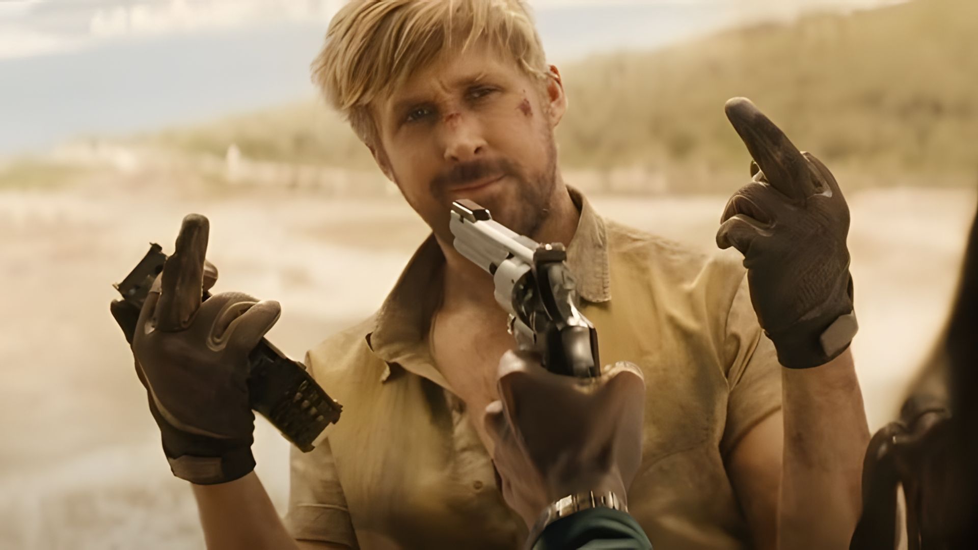Ryan Gosling with a bruised face makes an obscene gesture while a gun is pointed at his face