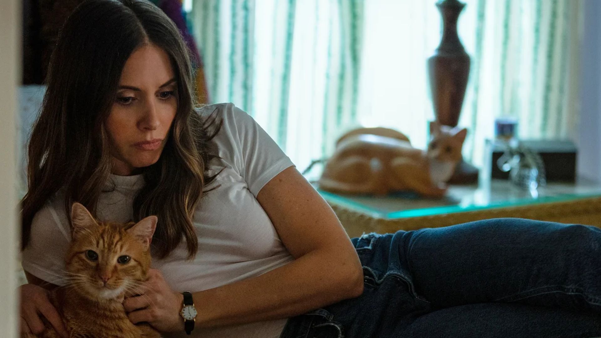 Alison Brie lies on a bed with a cat in her arms