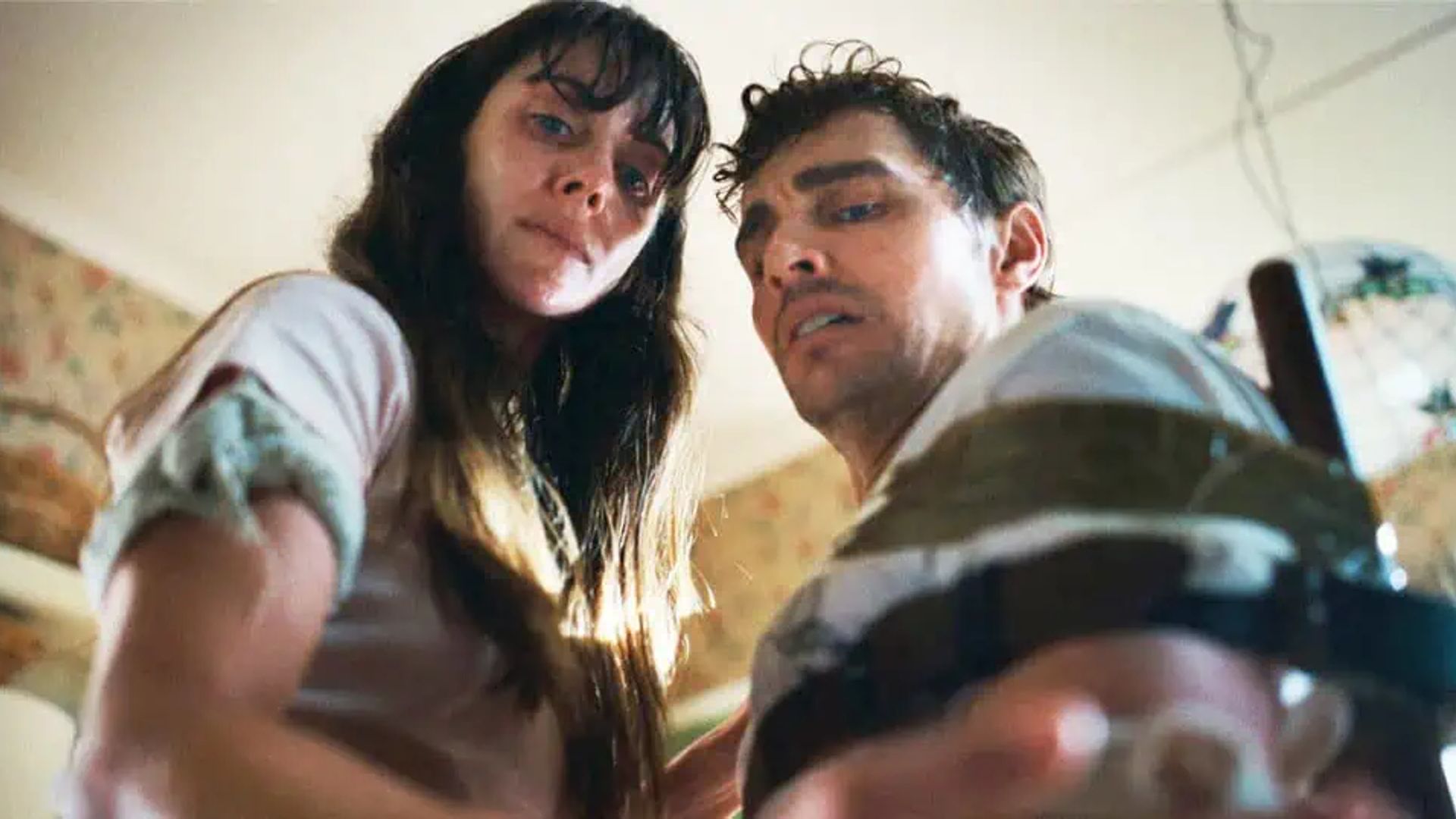 Dave Franco and Alison Brie look down at the camera with weary expressions on their faces