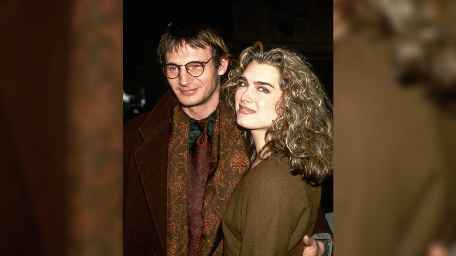 Liam Neeson and Brooke Shields in their youth, embracing and walking forward